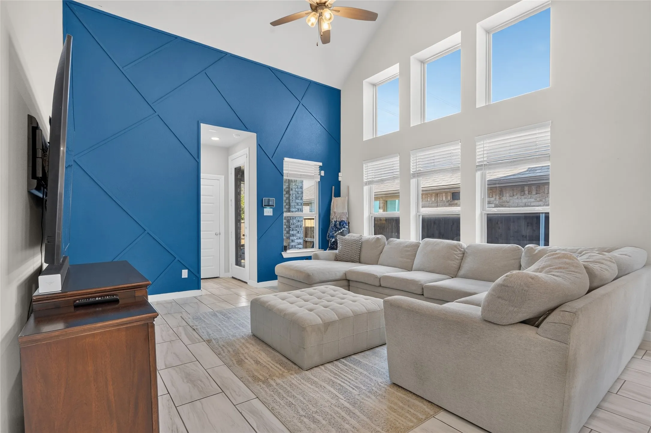 Vaulted ceiling with a ceiling fan, geometric accent wall, rectangular window array, and wood-finish tile flooring