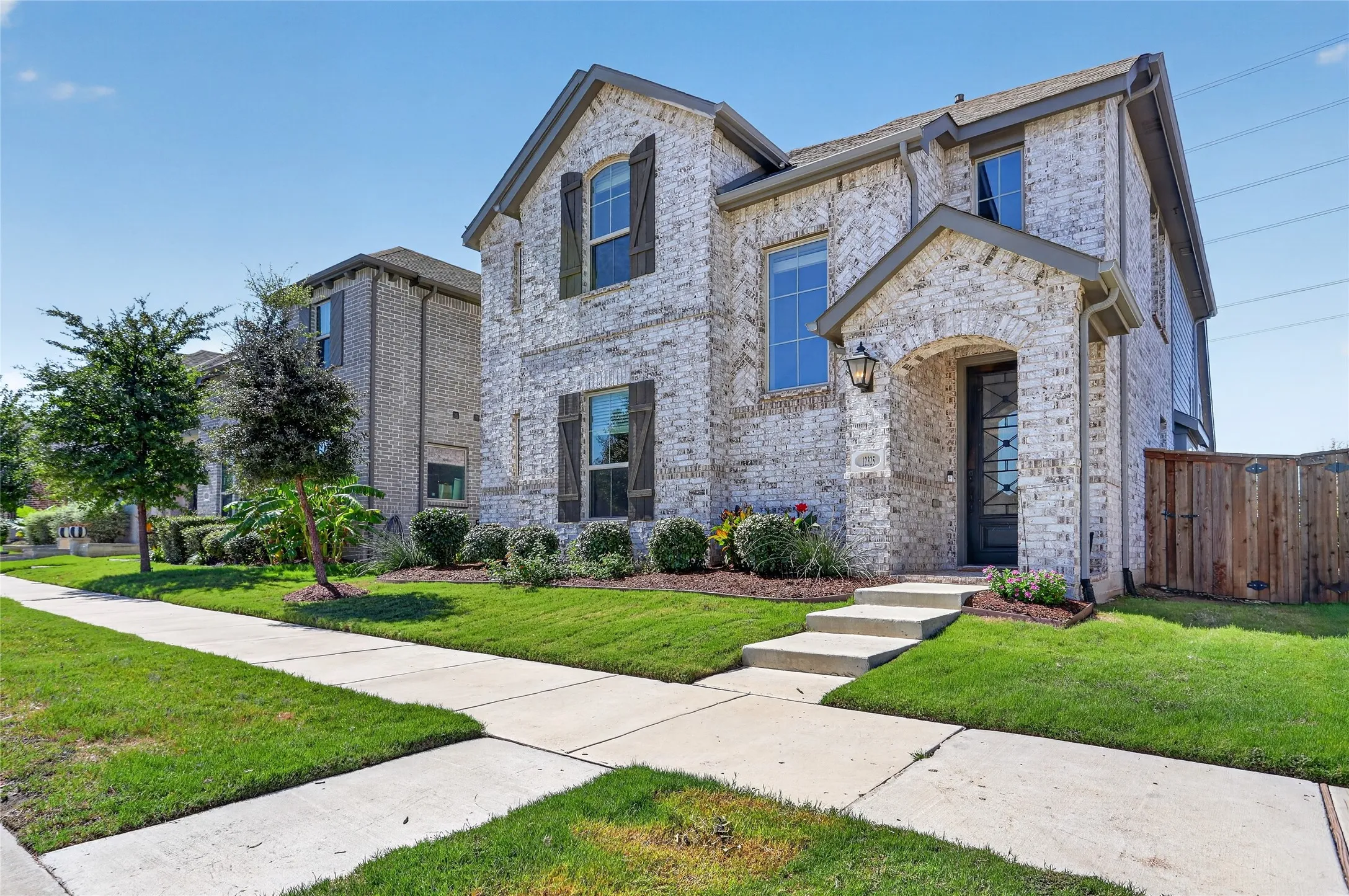 Two-story brick exterior with dark shutters, covered entry, front landscaping, and a wood privacy fence