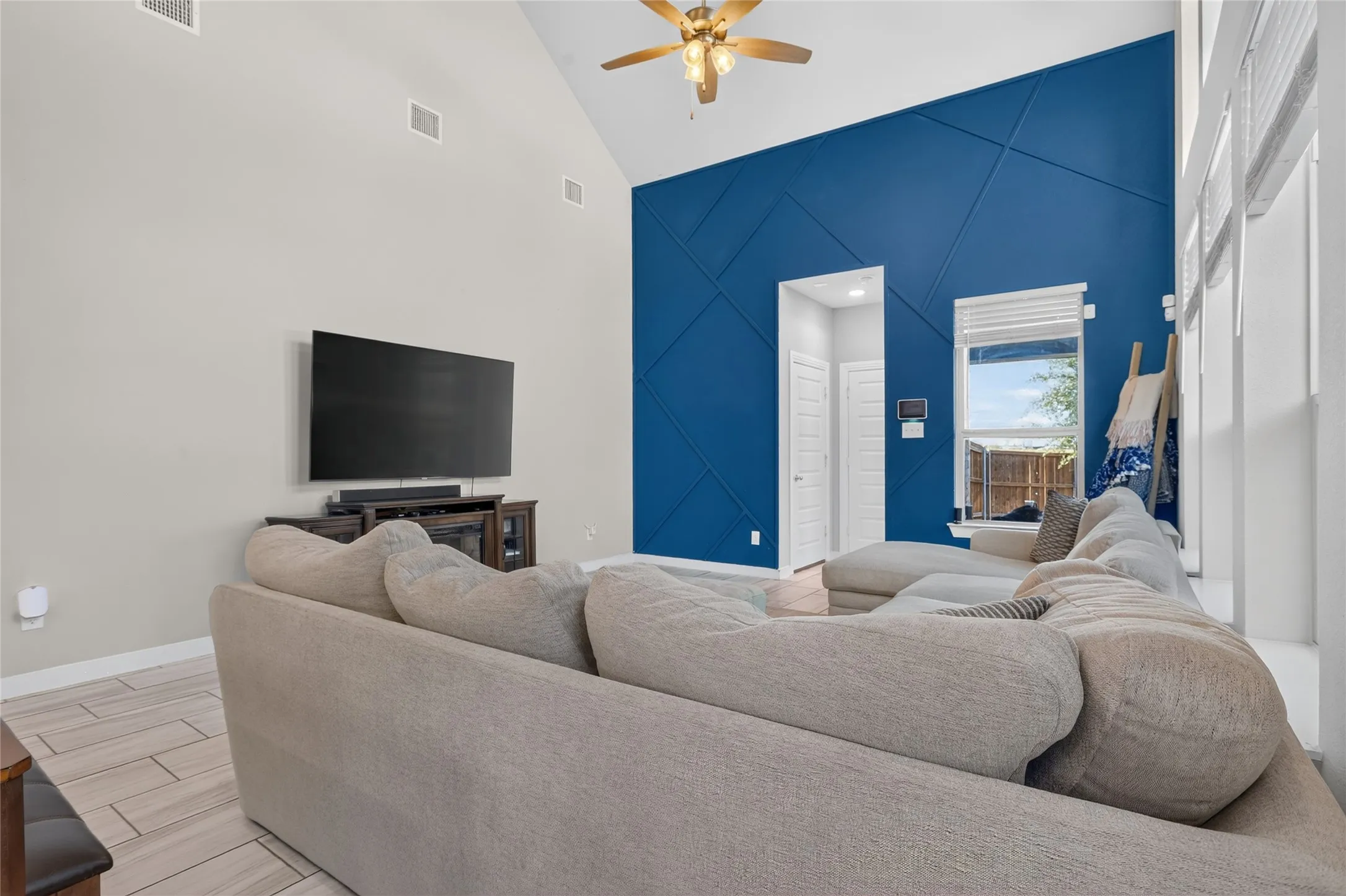 Vaulted ceiling with a ceiling fan, geometric accent wall, and wood-finish tile flooring
