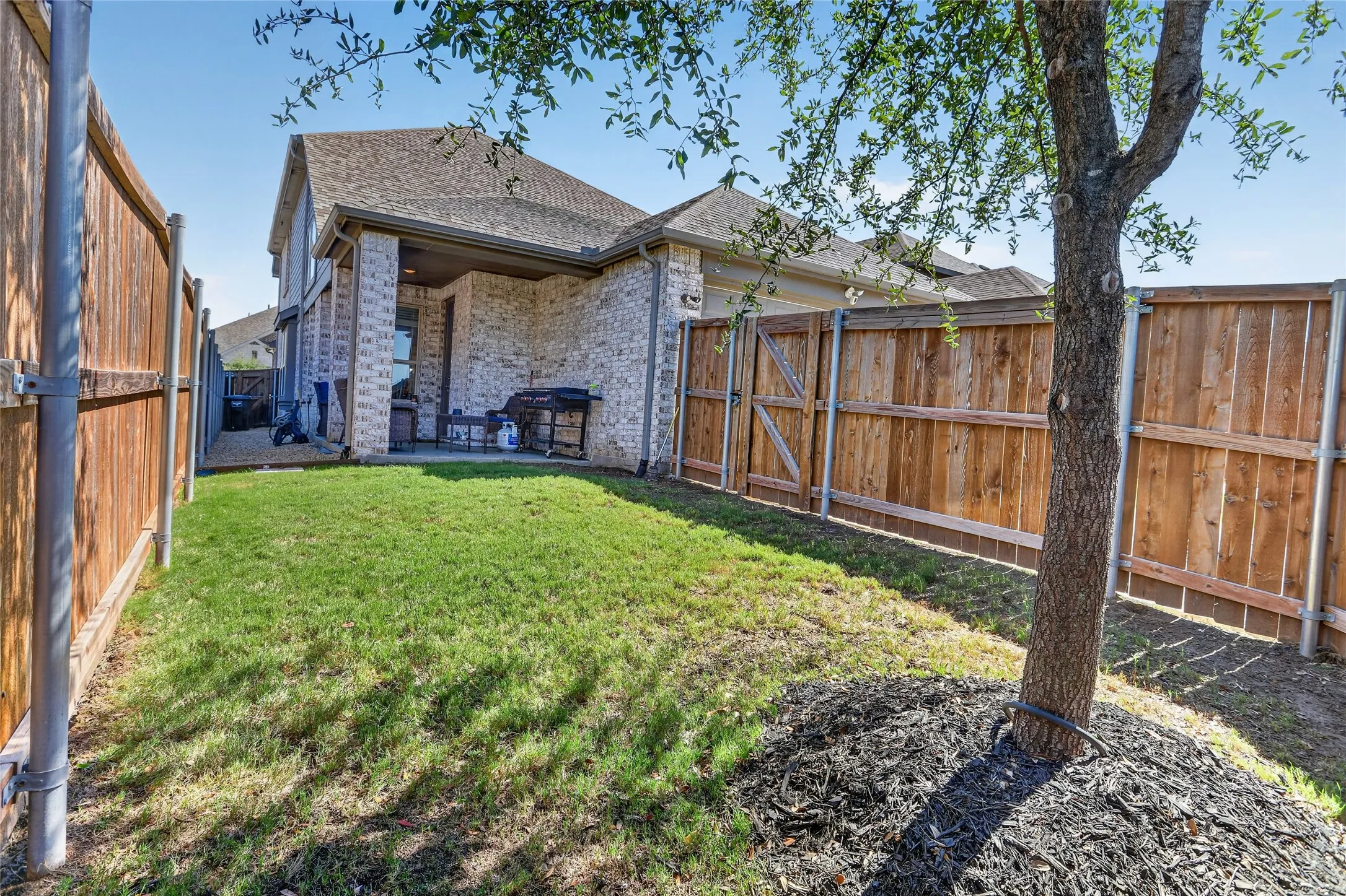 Manicured lawn, wood fencing, covered patio, and brick exterior