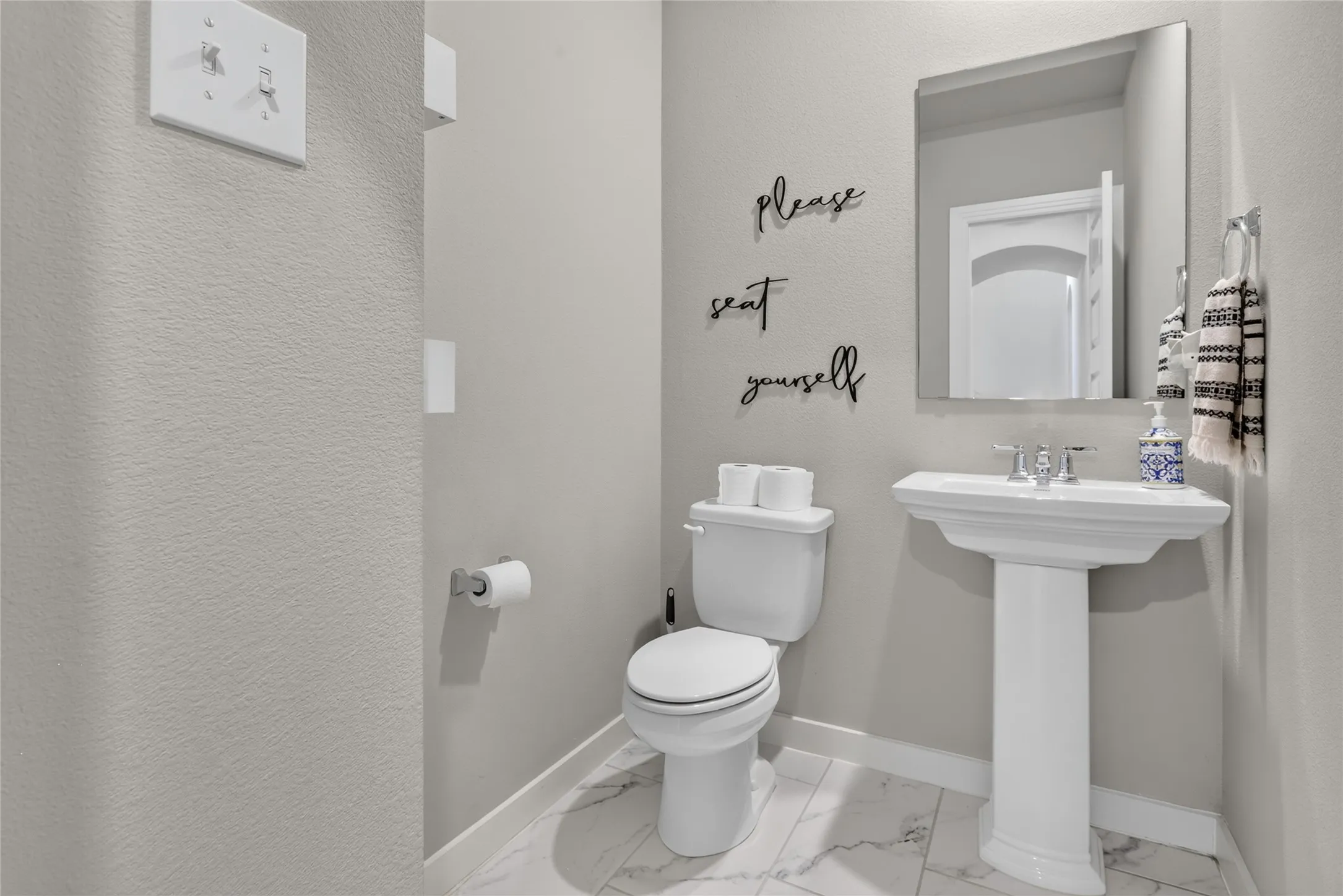 Pedestal sink with chrome fixtures, rectangular wall-mounted mirror, white toilet, and marble-look flooring