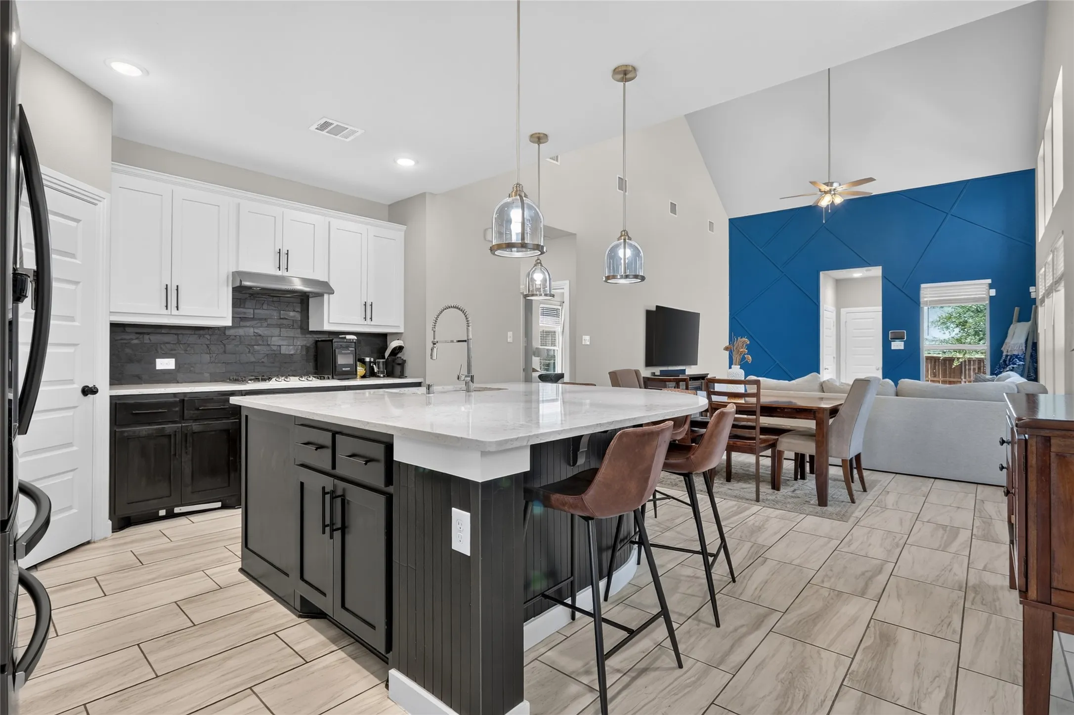 Spacious kitchen featuring an island with pendant lighting, white cabinetry, dark lower cabinetry, and a dark tile backsplash