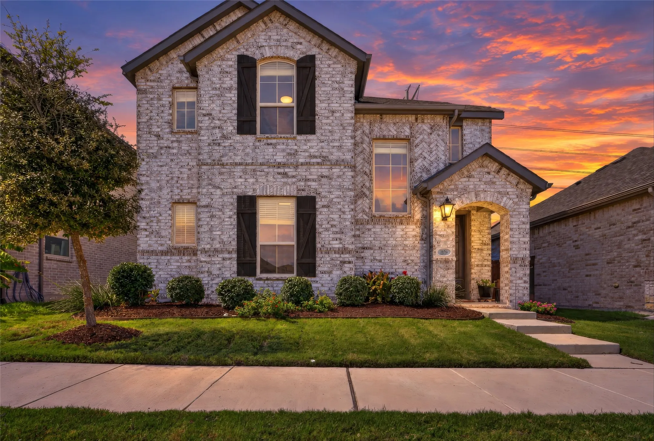 Two-story brick exterior with dark shutters, arched entry, and well-maintained landscaping