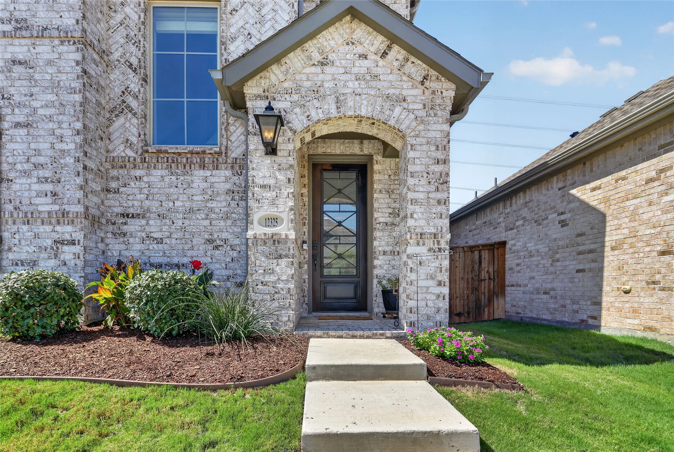 Brick exterior with arched entryway, decorative front door, and overhead outdoor lighting