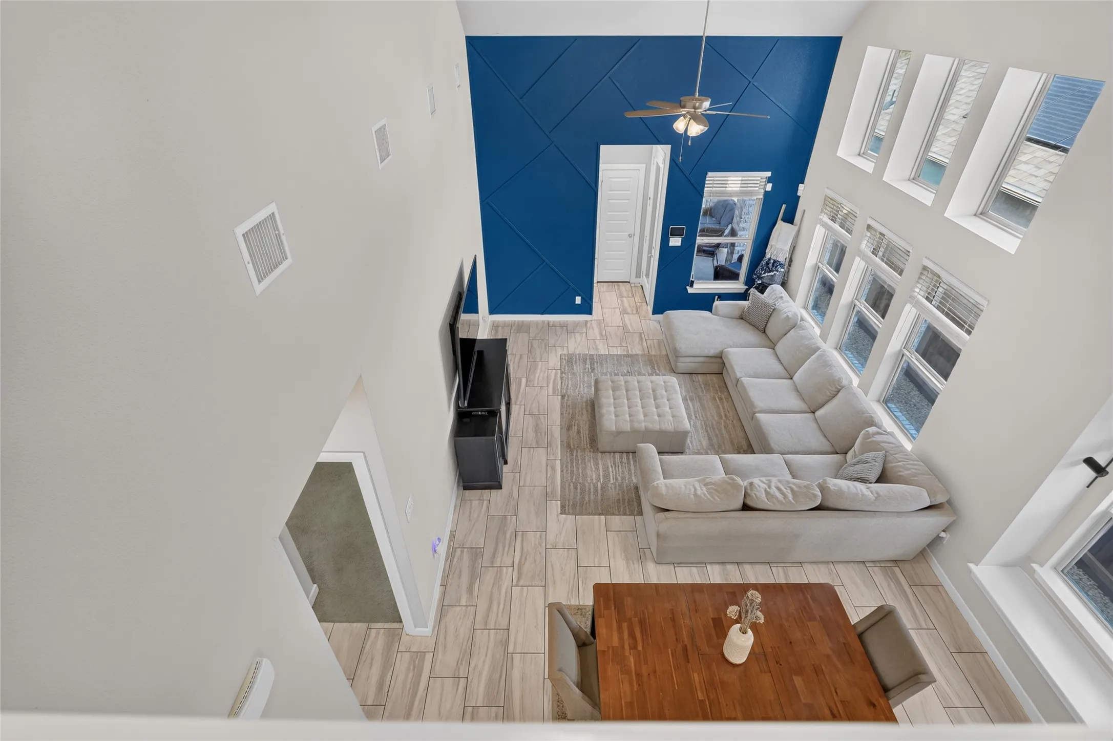 Two-story living area with high ceilings, a decorative blue accent wall, wood-finish tile flooring, and multiple large windows