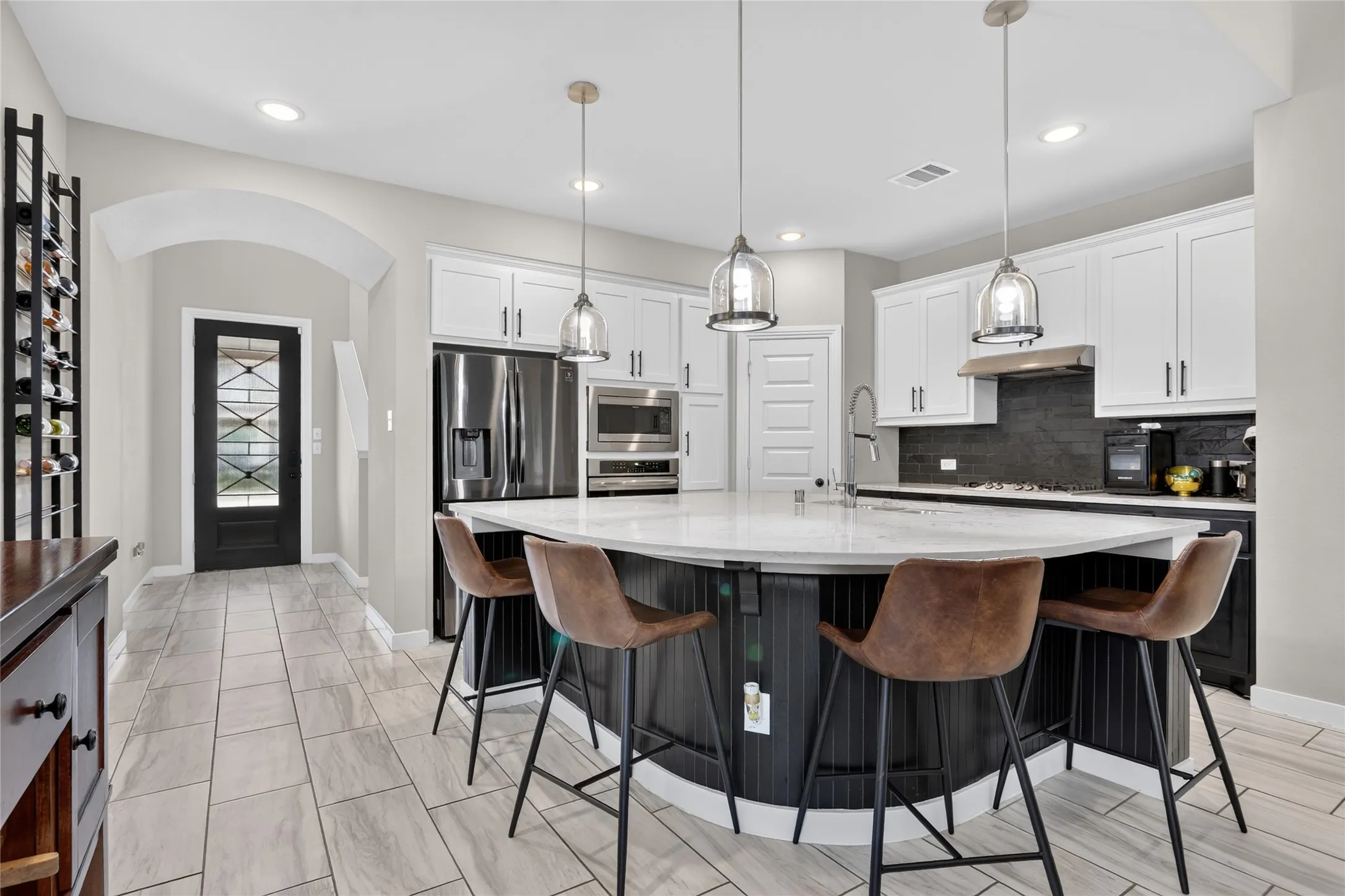 Kitchen featuring white upper cabinetry, black lower cabinetry, stainless steel appliances, and a curved island with a light-toned countertop
