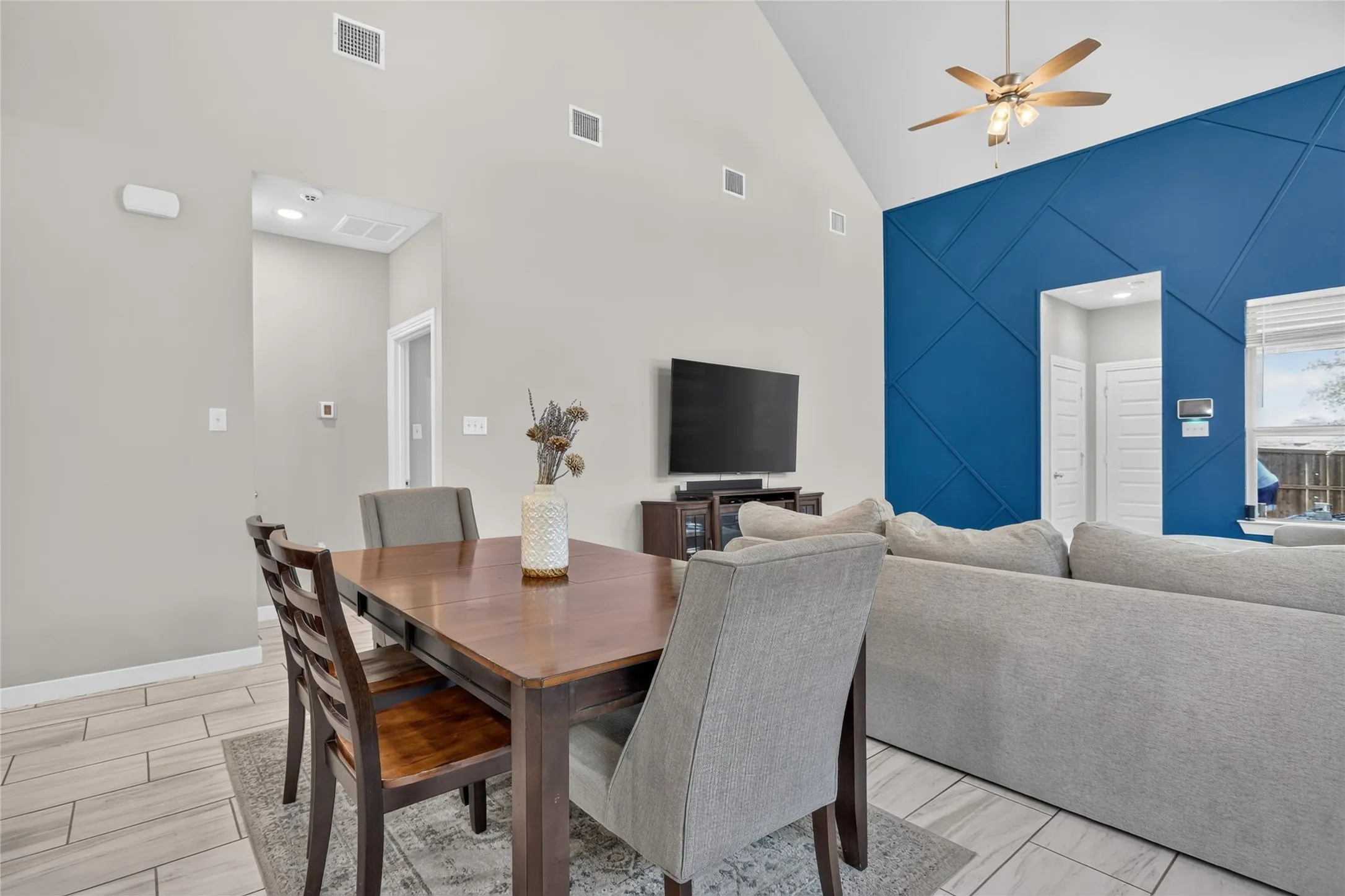 Vaulted ceiling with a ceiling fan, geometric accent wall, and wood-finish tile flooring