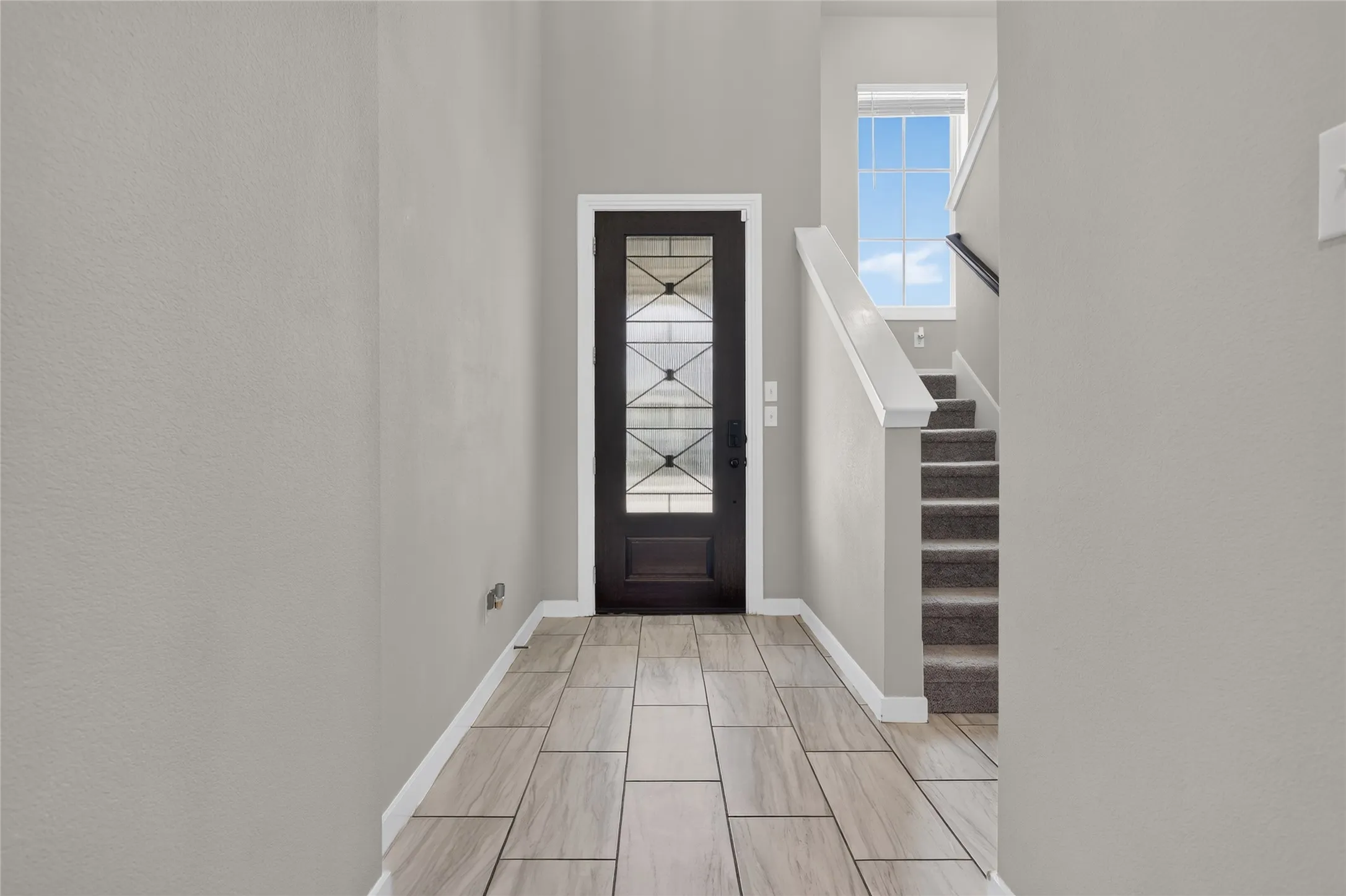 Foyer featuring wood-finish tile flooring, a decorative glass-paneled entry door, and a carpeted staircase with a window