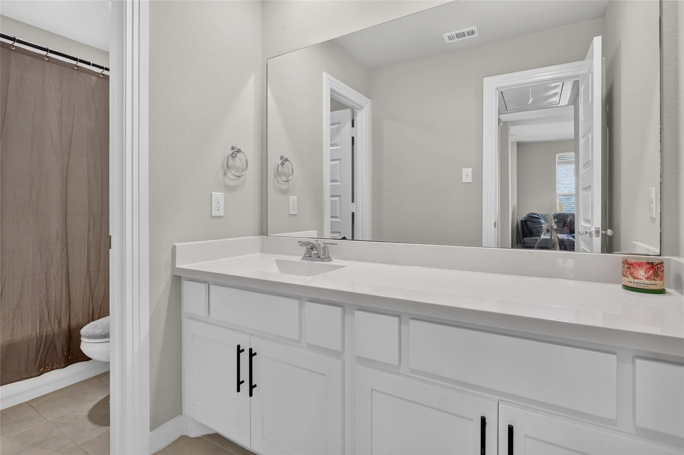 White vanity with black hardware, integrated sink, and expansive mirror