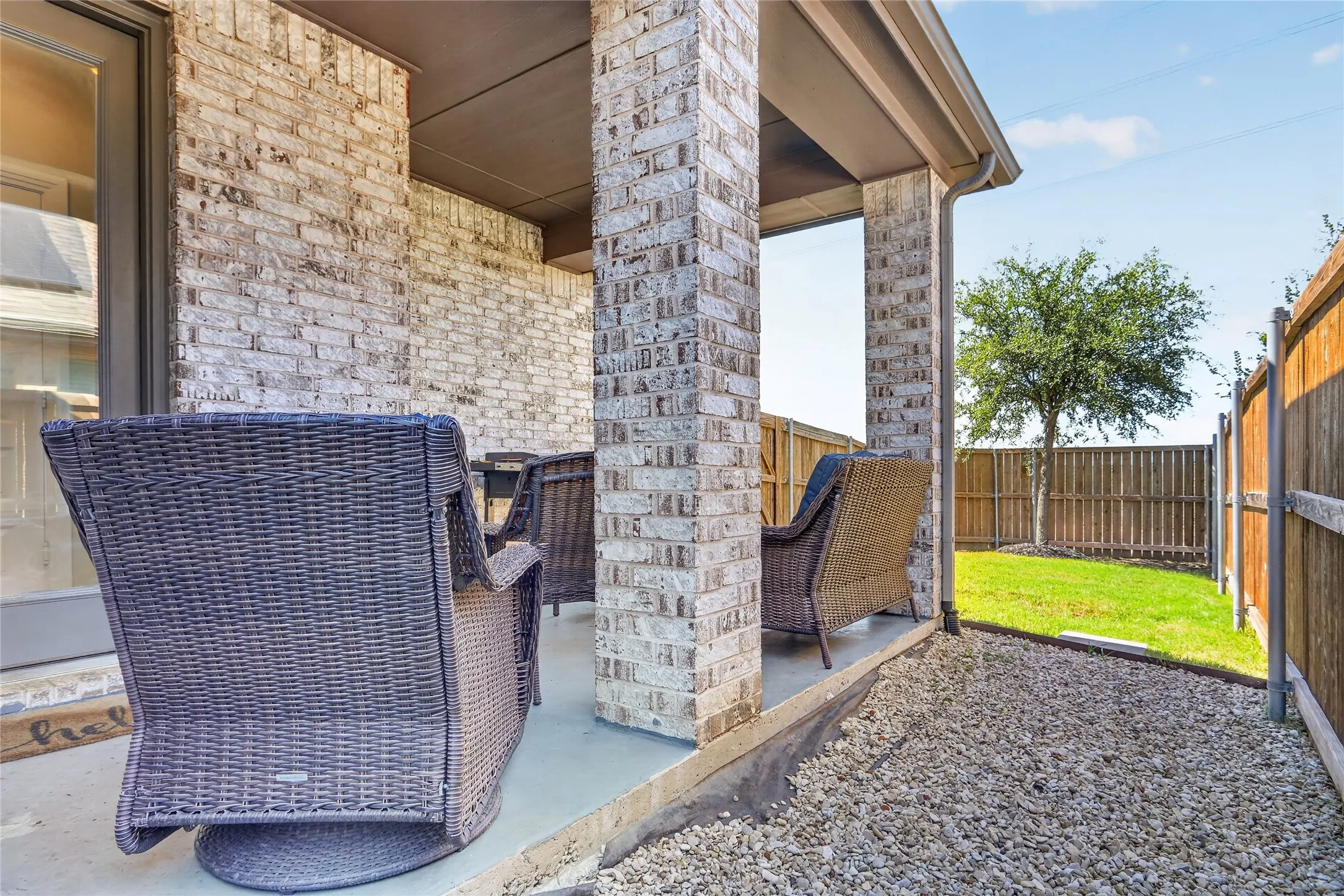 Covered patio with brick columns, concrete flooring, and a fenced backyard with a tree and grassy area