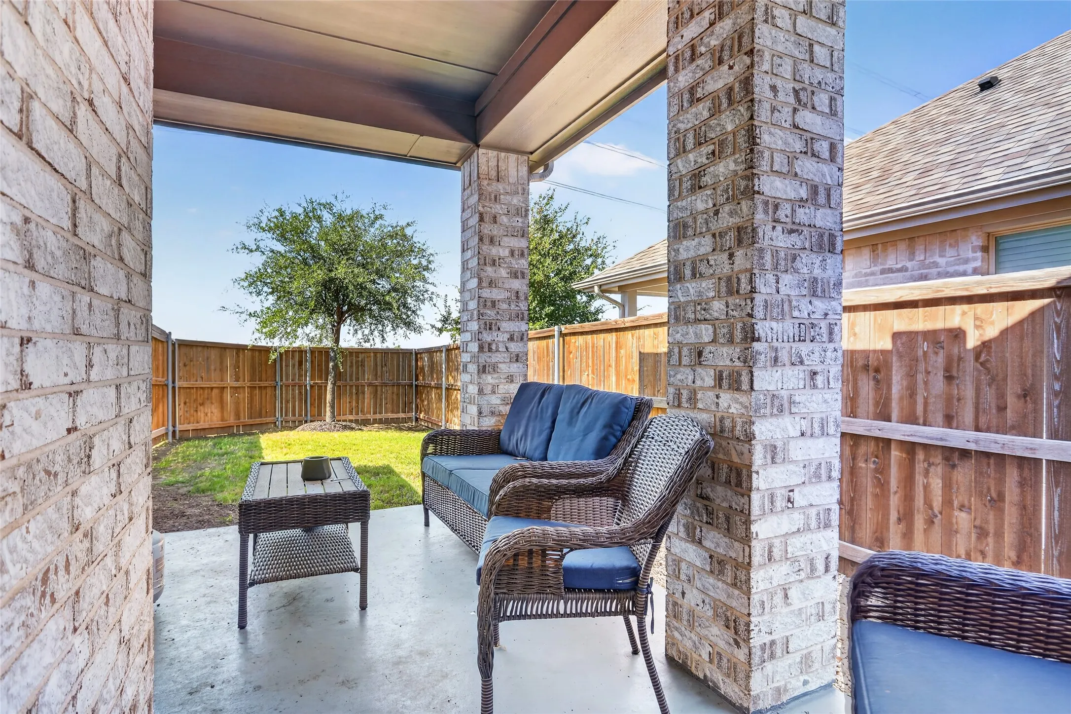 Covered patio featuring brick columns, concrete flooring, and a fully fenced yard with a tree