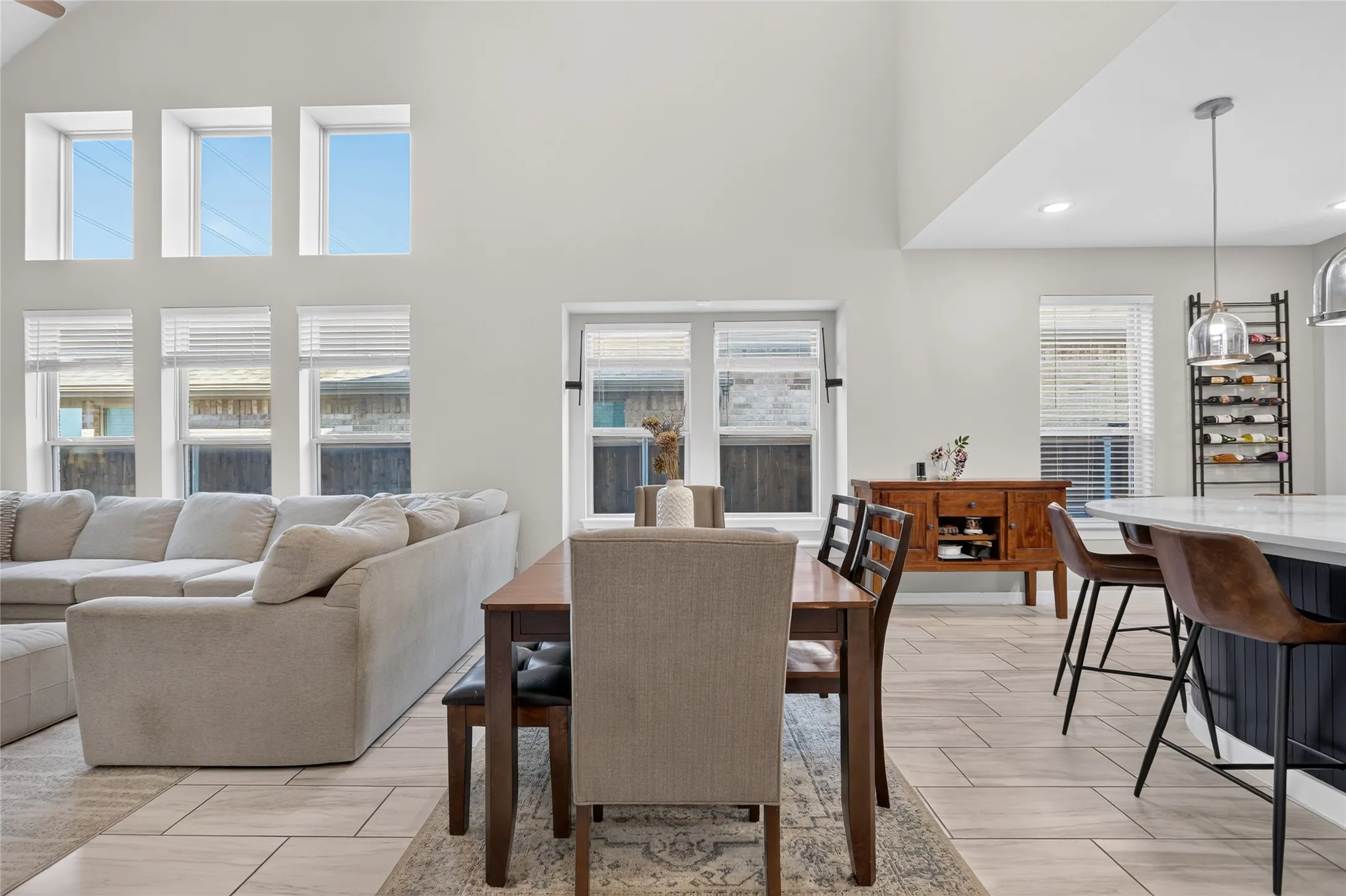 Vaulted ceilings, a dining area, a kitchen island with seating, pendant lighting, and light-toned tile flooring