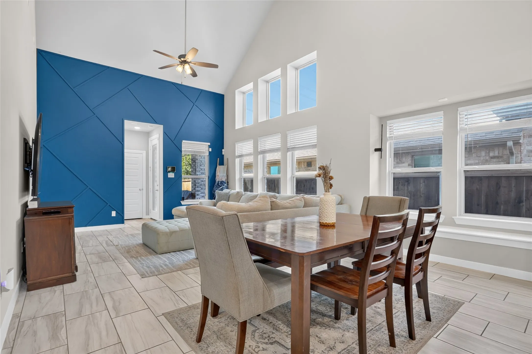 Vaulted ceiling with a ceiling fan, accent wall featuring geometric paneling, an array of windows providing abundant light, and wood-finish tile flooring