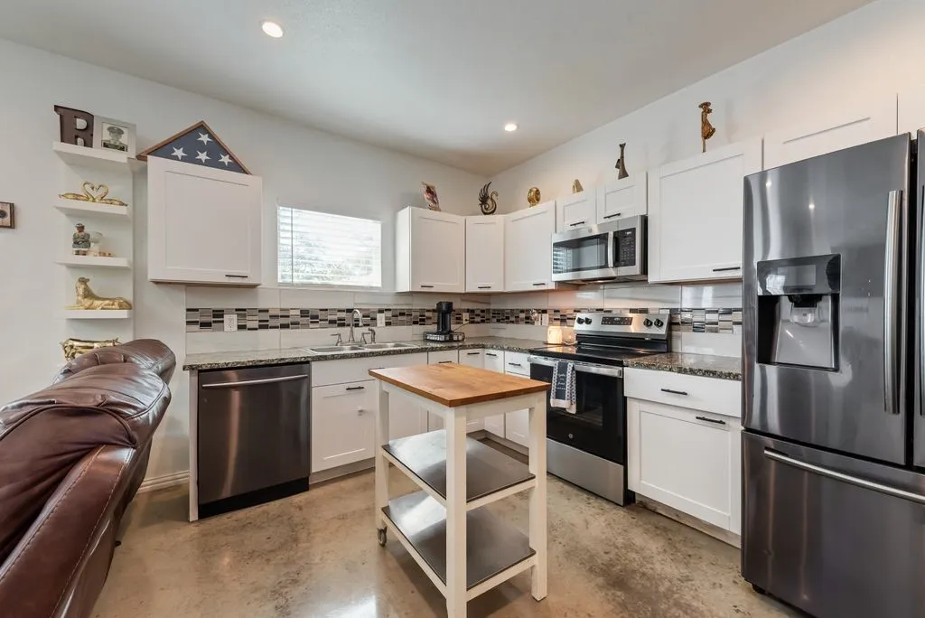 White cabinetry, stainless steel appliances, mosaic tile backsplash, granite countertops, and polished concrete flooring