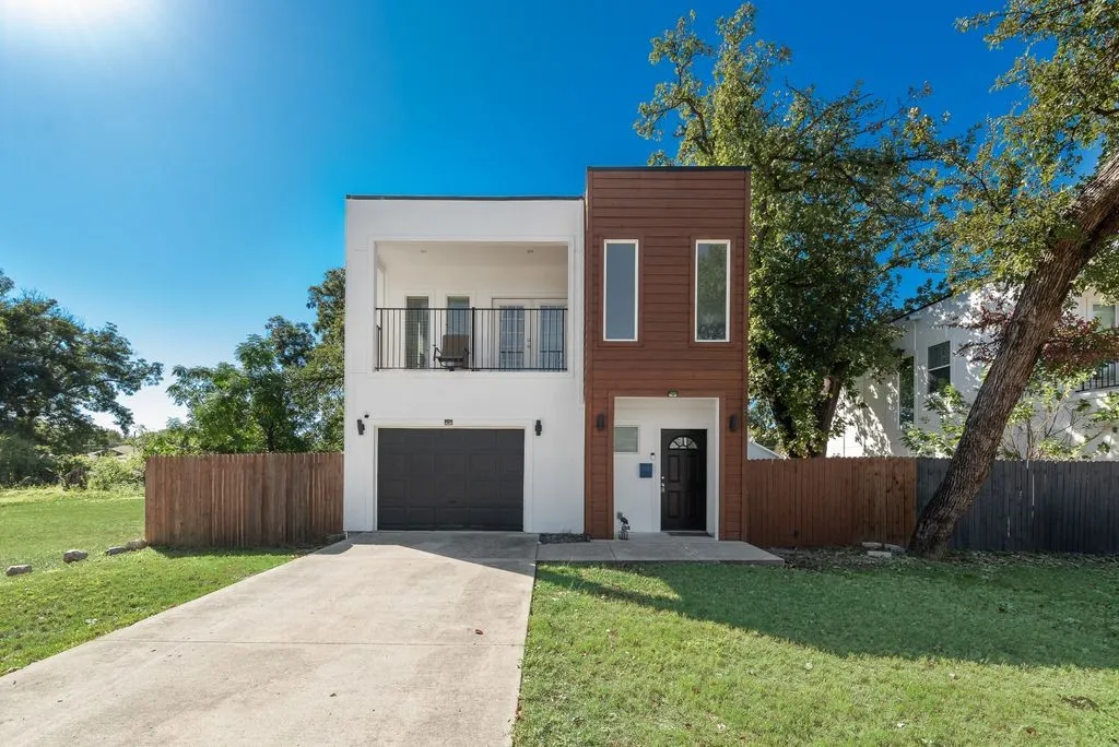Modern exterior with white and wood-finish siding, an integrated garage, a second-story balcony with iron railing, and a concrete driveway