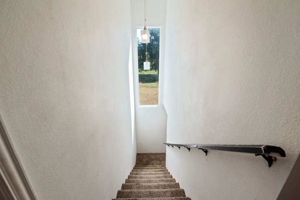 Stairwell with a window, textured wall finish, and a dark-toned handrail