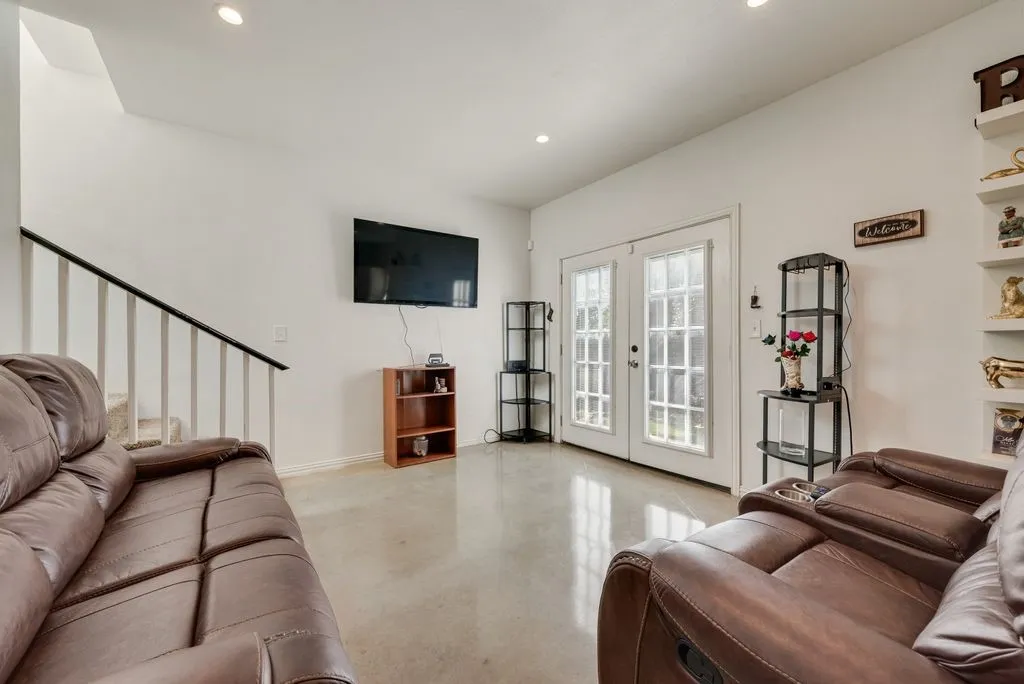 Recessed lighting, light-toned flooring, staircase with dark handrail and white balusters, and white French doors with divided lites