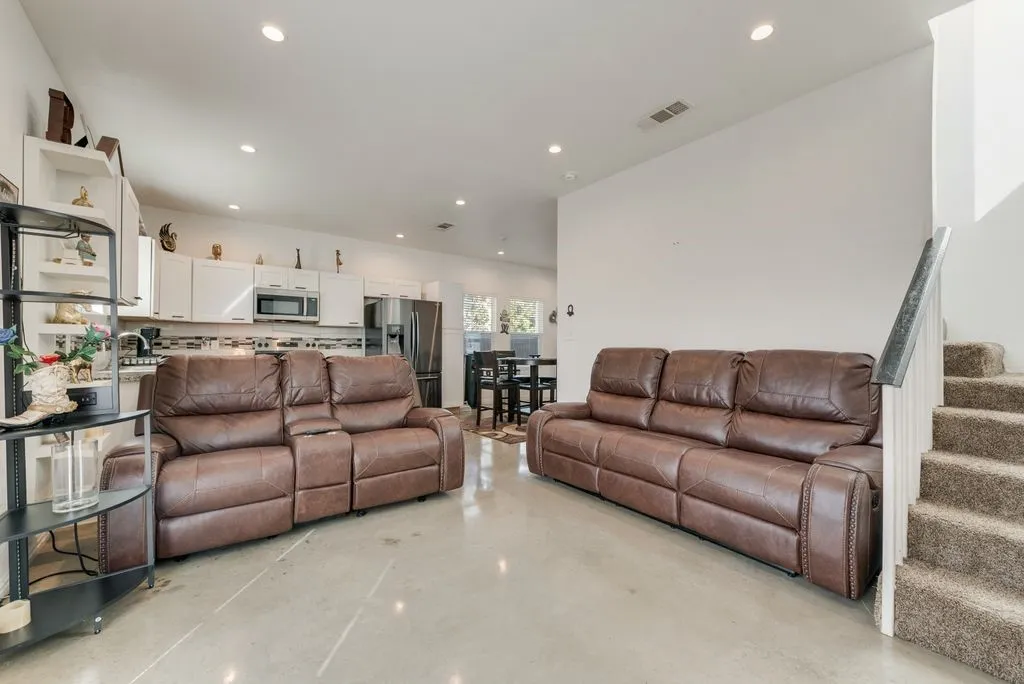 Open-concept living space featuring concrete flooring, recessed lighting, and a white kitchen with stainless steel appliances