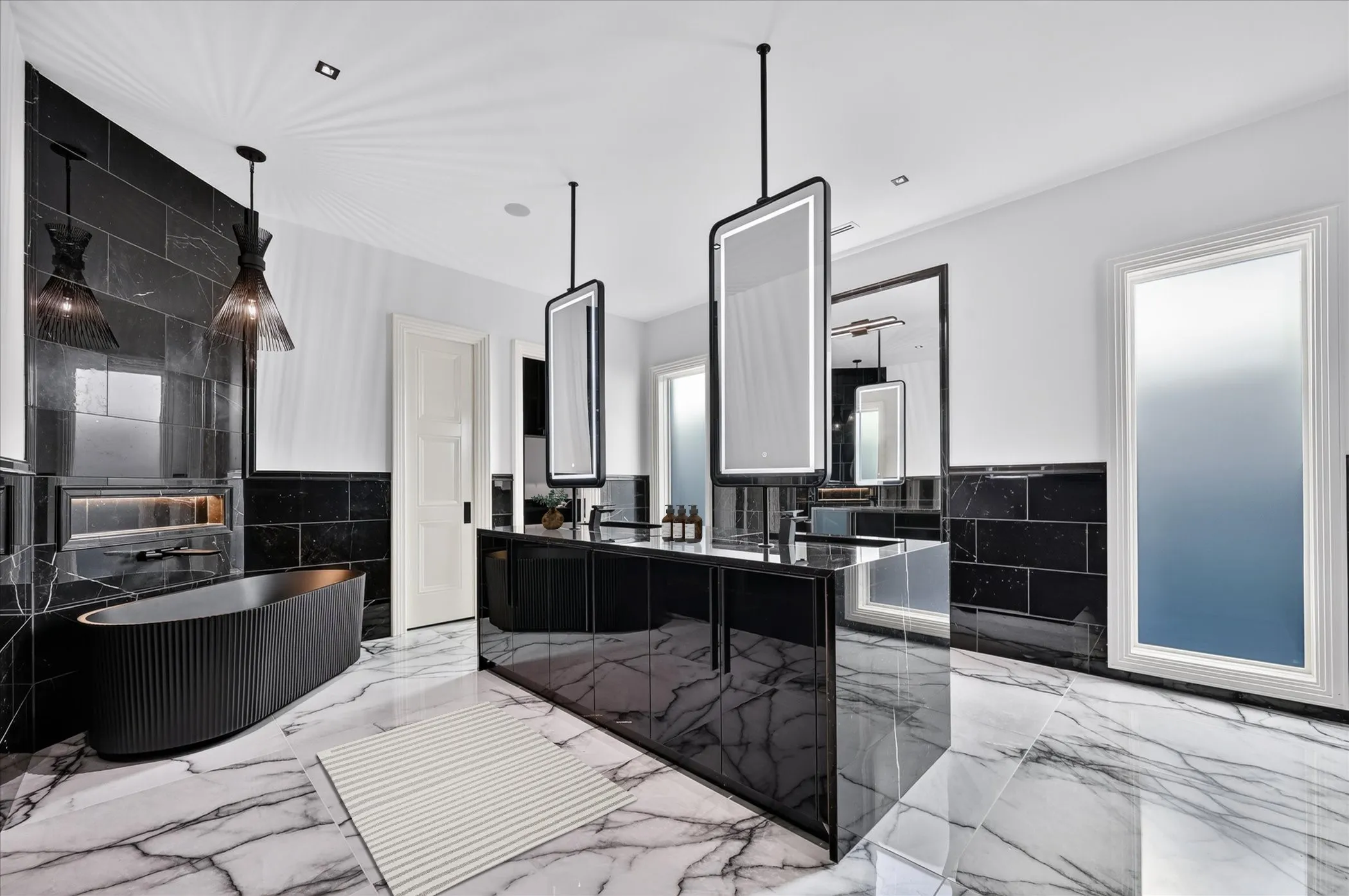 Freestanding soaking tub, floor-to-ceiling black stone-finish wall, dual vanity with integrated sinks, illuminated mirrors, and white marble-look flooring