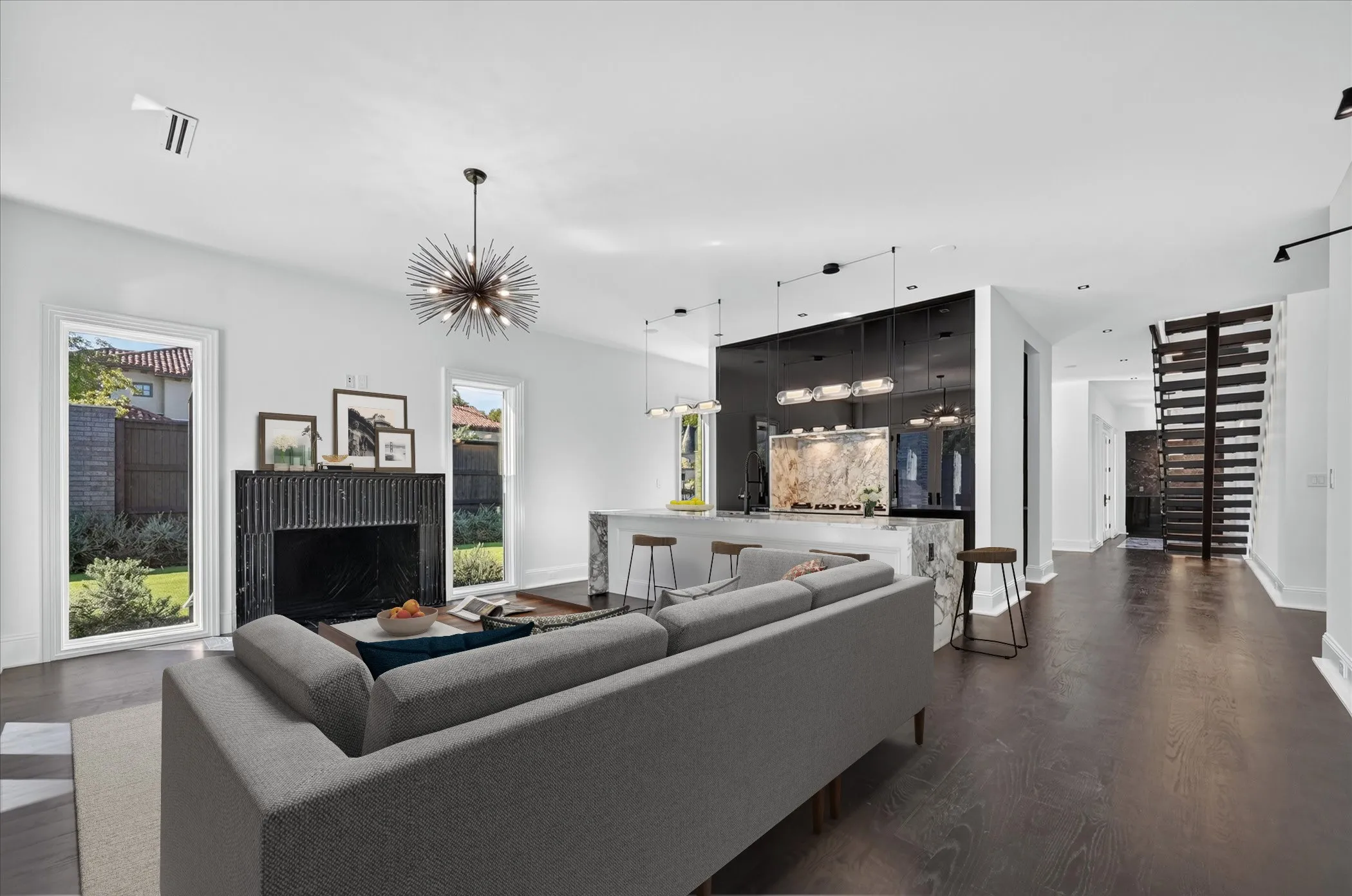 Open-concept living space featuring wood-finish flooring, a modern black fireplace, an island with stone countertops, and a unique open staircase design
