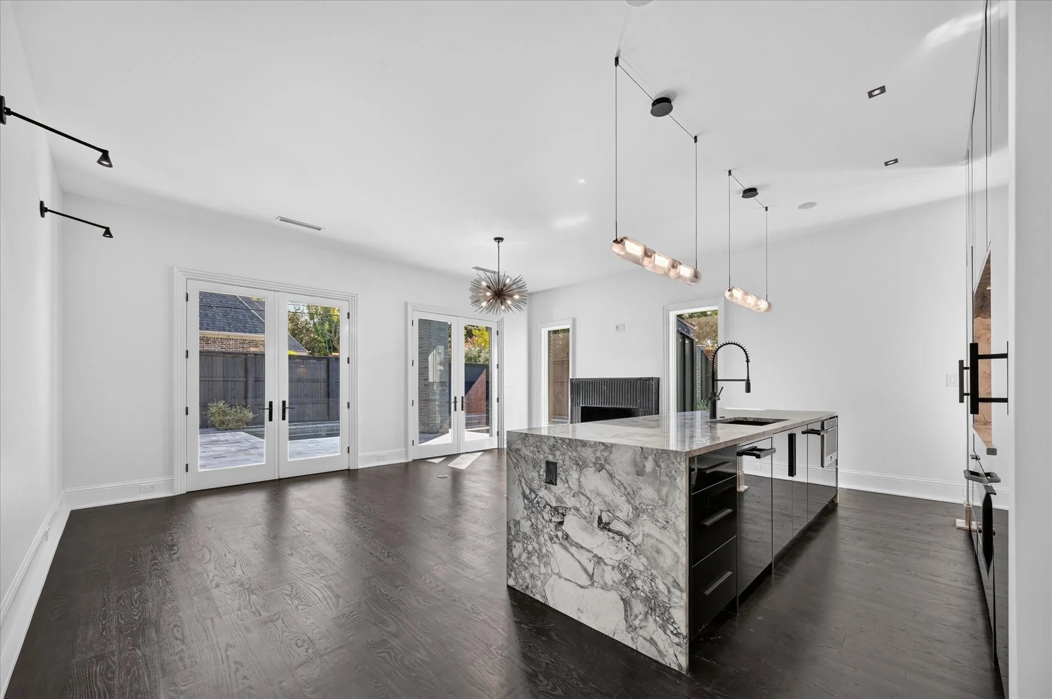 Spacious room with dark wood-finish flooring, multiple sets of white French doors, and a kitchen island featuring a waterfall stone countertop and integrated sink