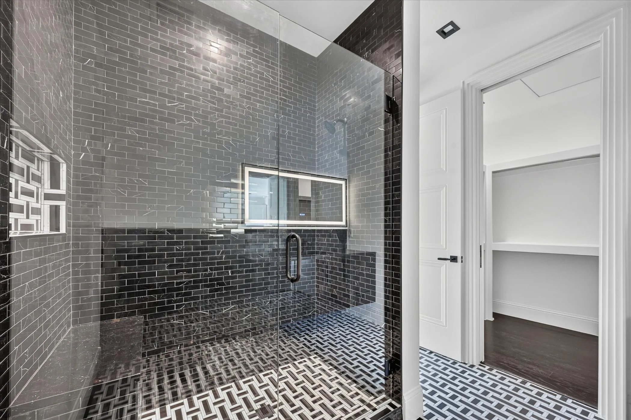 Glass-enclosed shower with black subway tile, mosaic floor tile, and a built-in shower niche
