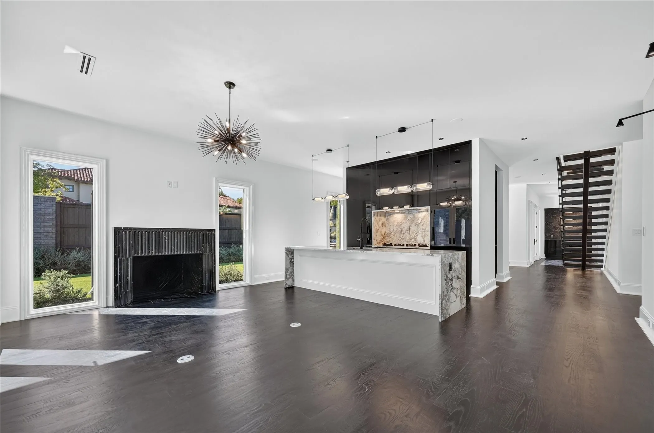 Dark wood-finish flooring, a fluted black fireplace surround, and a white stone kitchen island with a waterfall edge