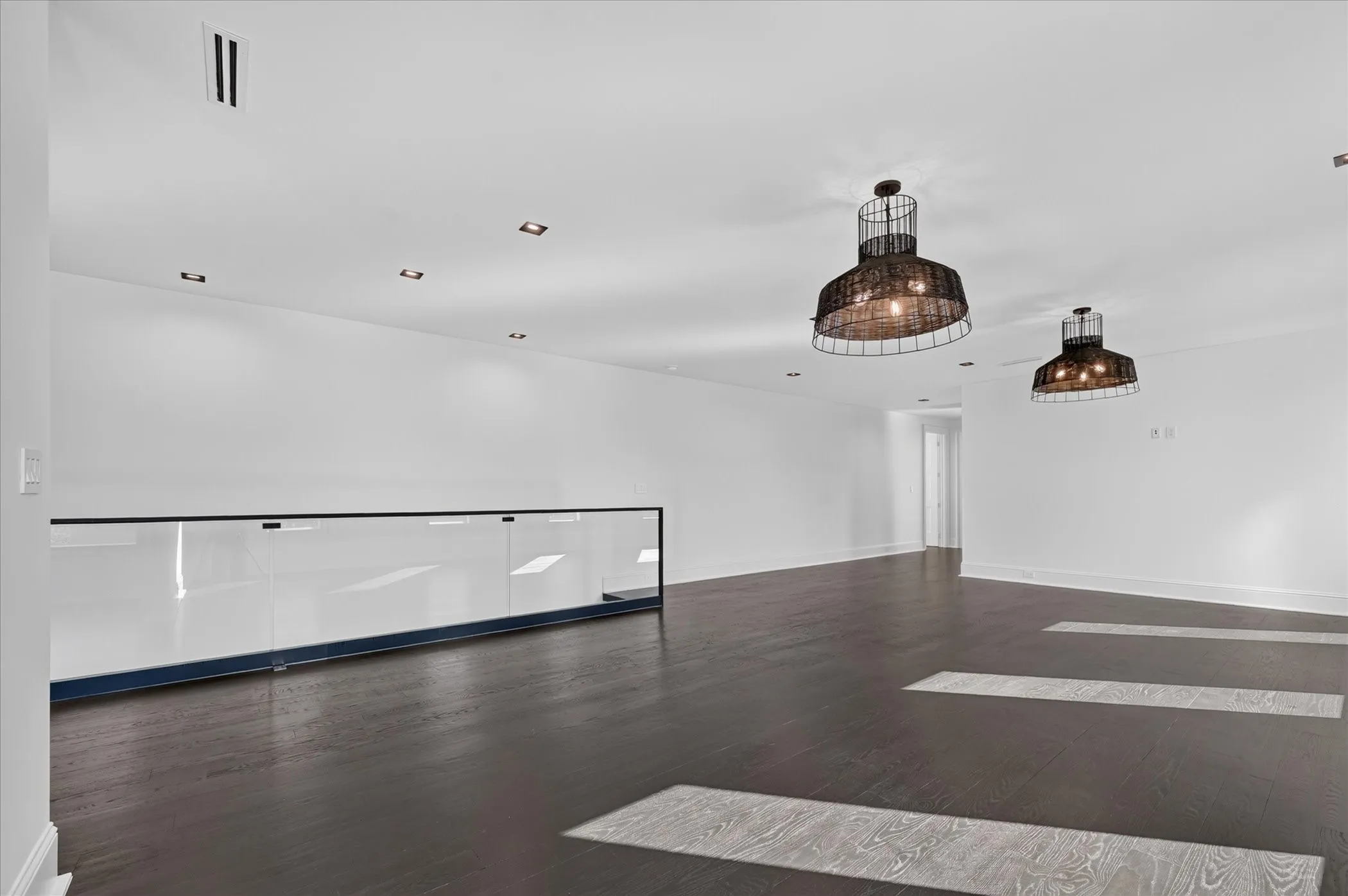 Dark wood-finish flooring, recessed lighting, and modern wire-cage pendant lights