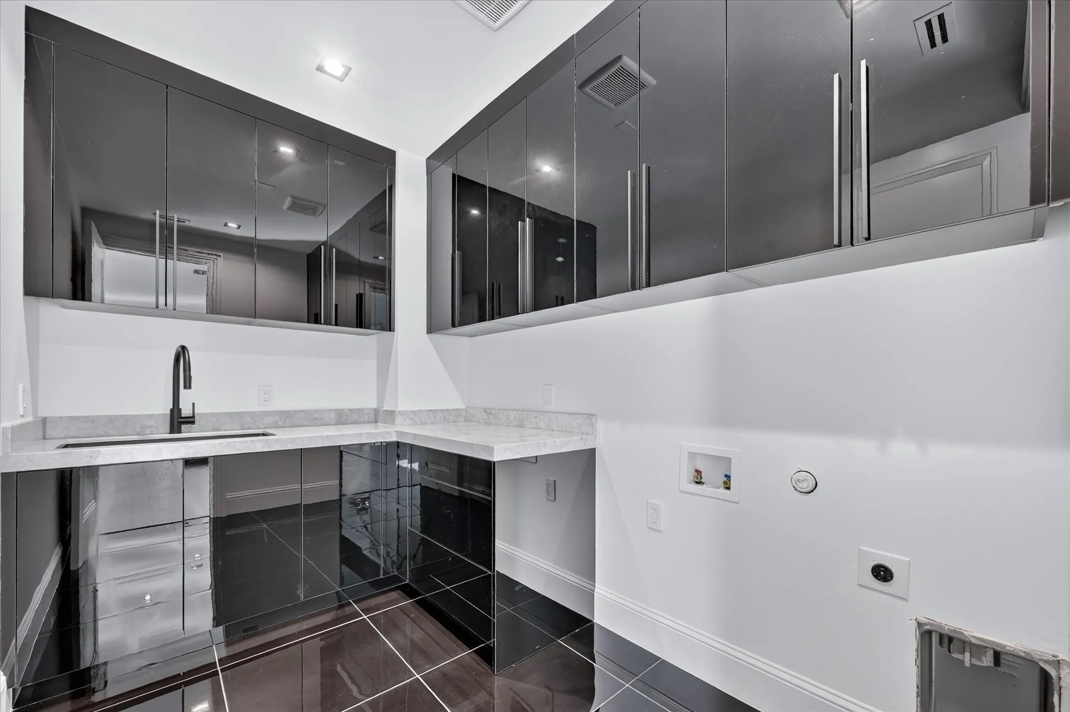 Glossy black cabinetry, white countertops, built-in sink with a black faucet, and dark tile flooring