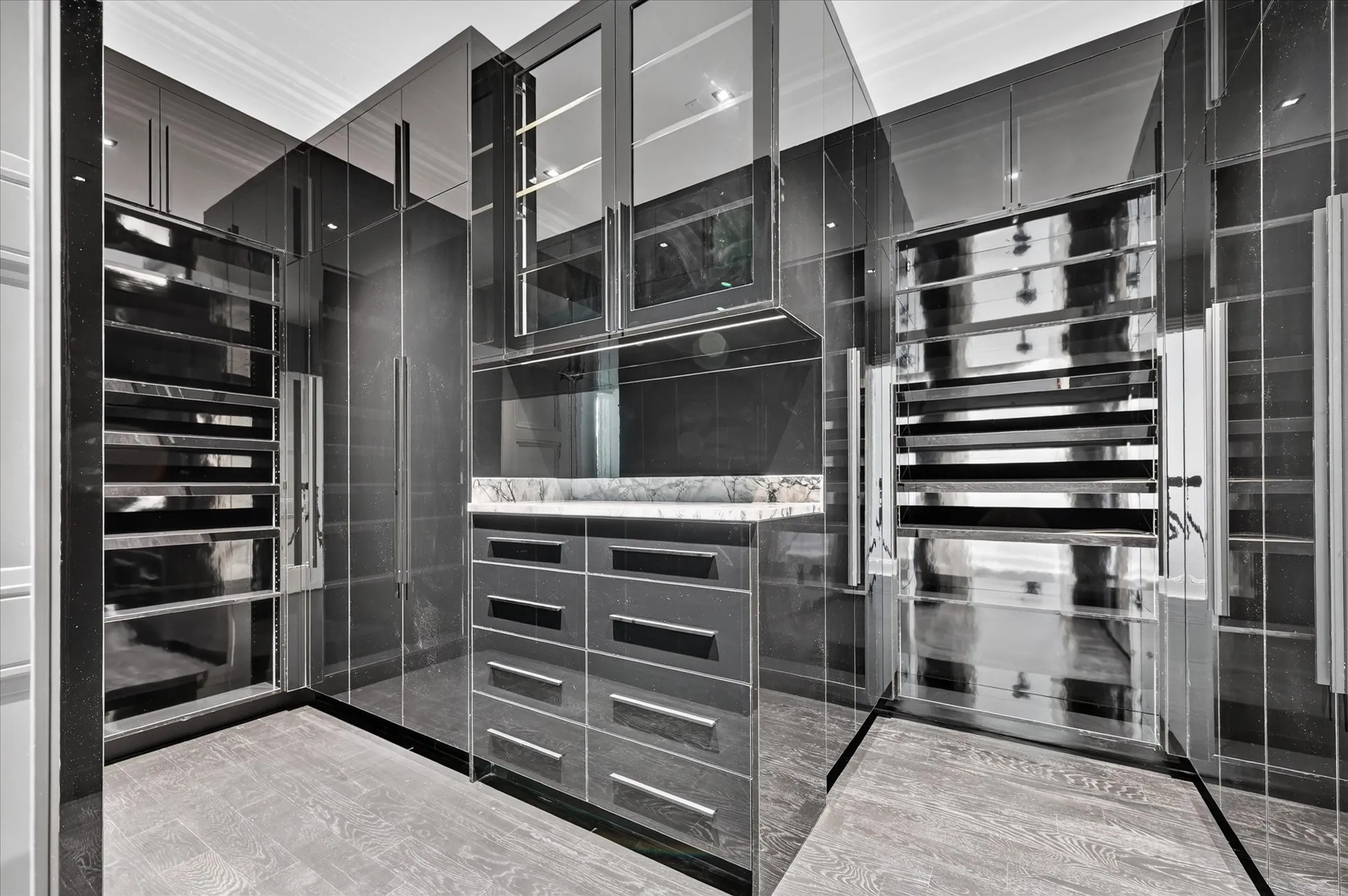 Custom built-in cabinetry with glass-front uppers, a central vanity with a stone countertop, wood-finish flooring, and integrated display shelving