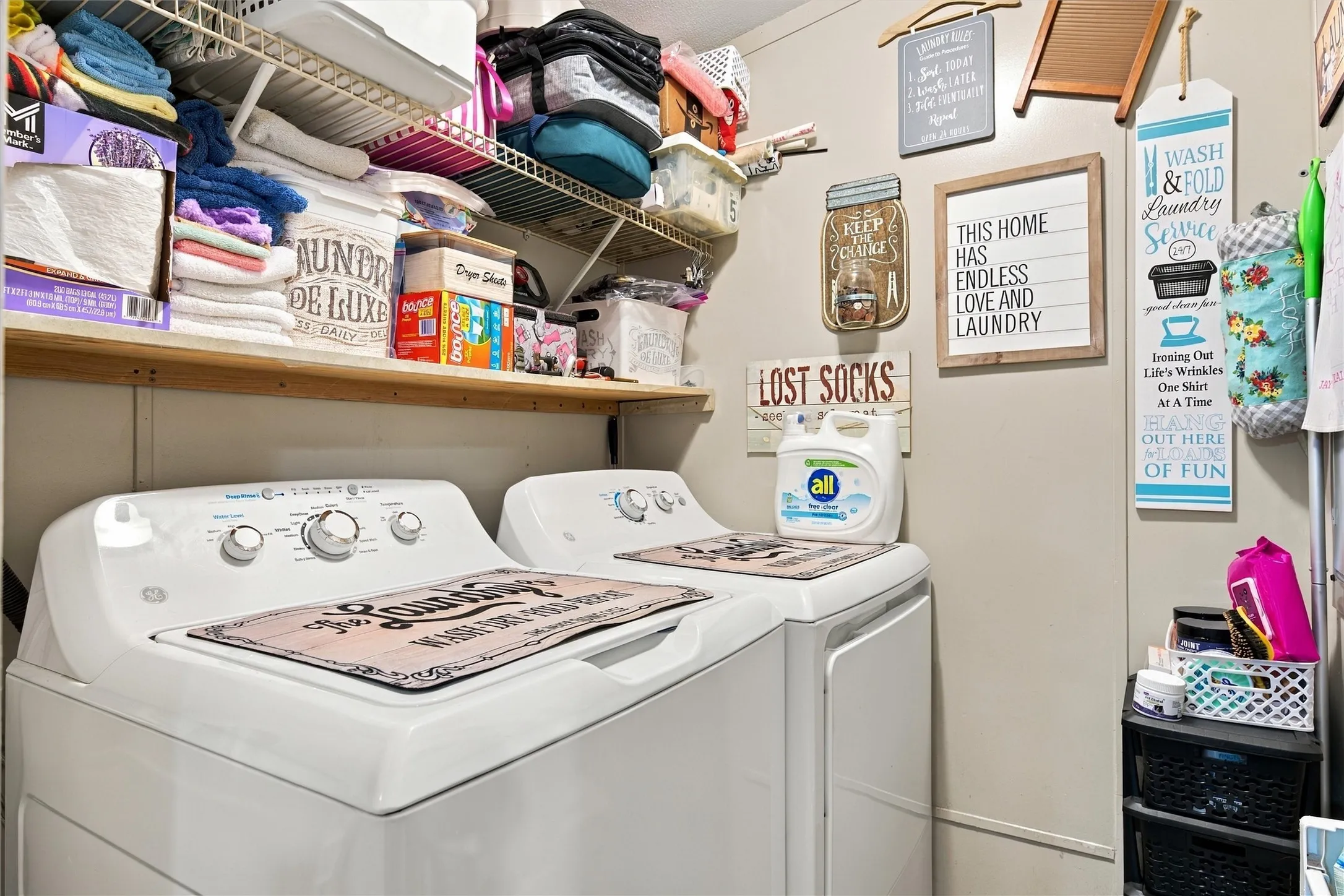 White washer and dryer units with overhead shelving and a wall-mounted shelf