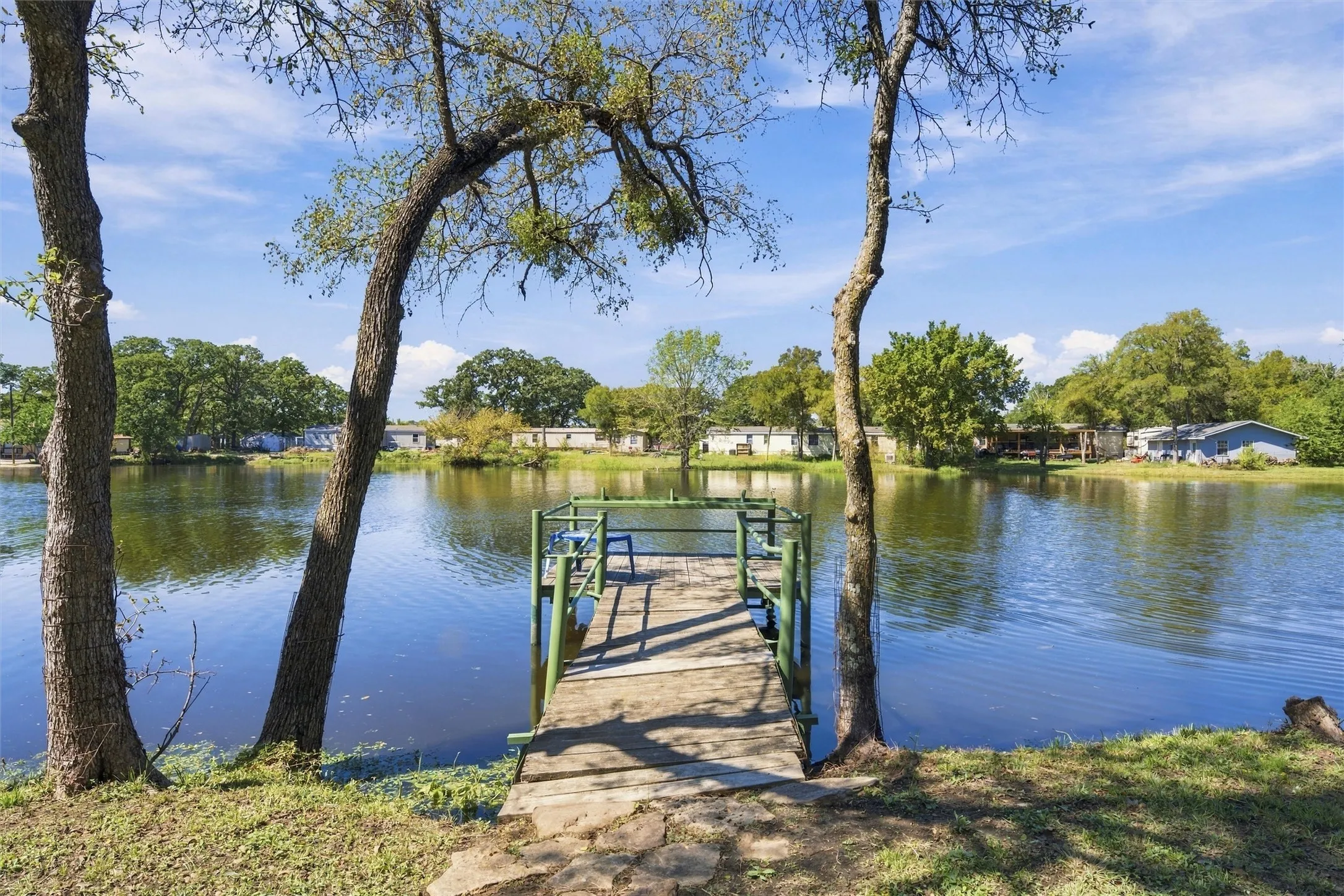 Private dock with wood planking and green railings, situated on a tranquil body of water