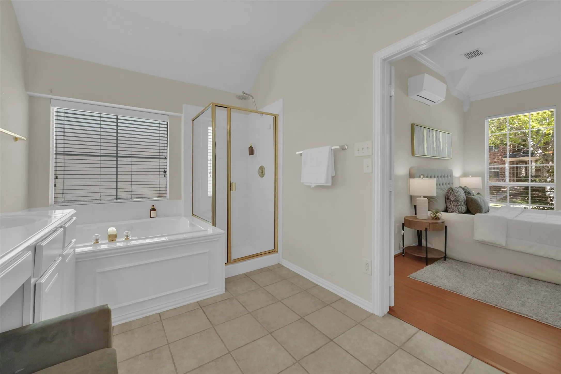 Soaking tub with a window, glass-enclosed shower with gold-toned fixtures, and a white vanity with integrated sink