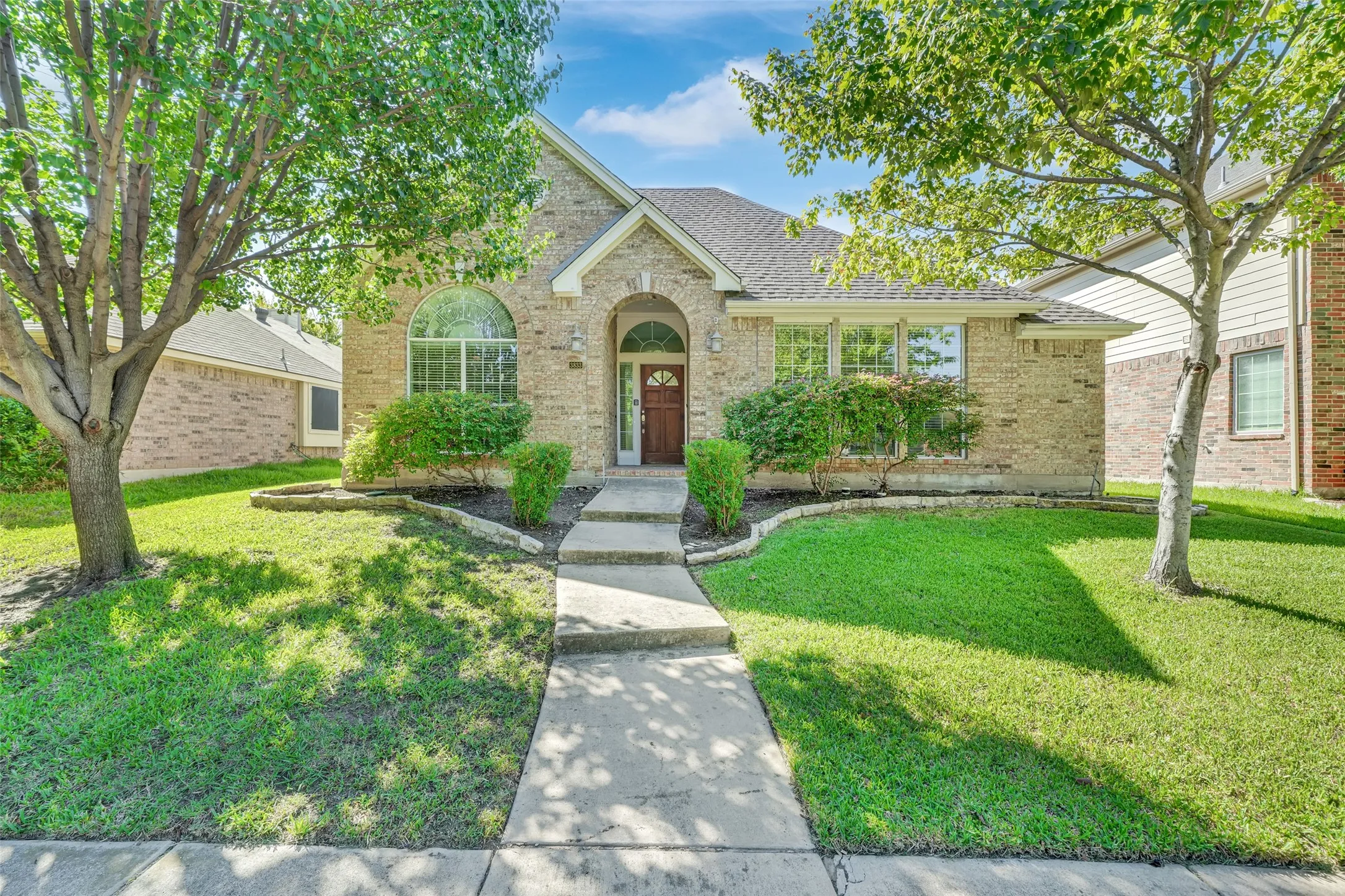 Brick exterior with an arched entryway, mature landscaping, and a concrete pathway leading to the front door
