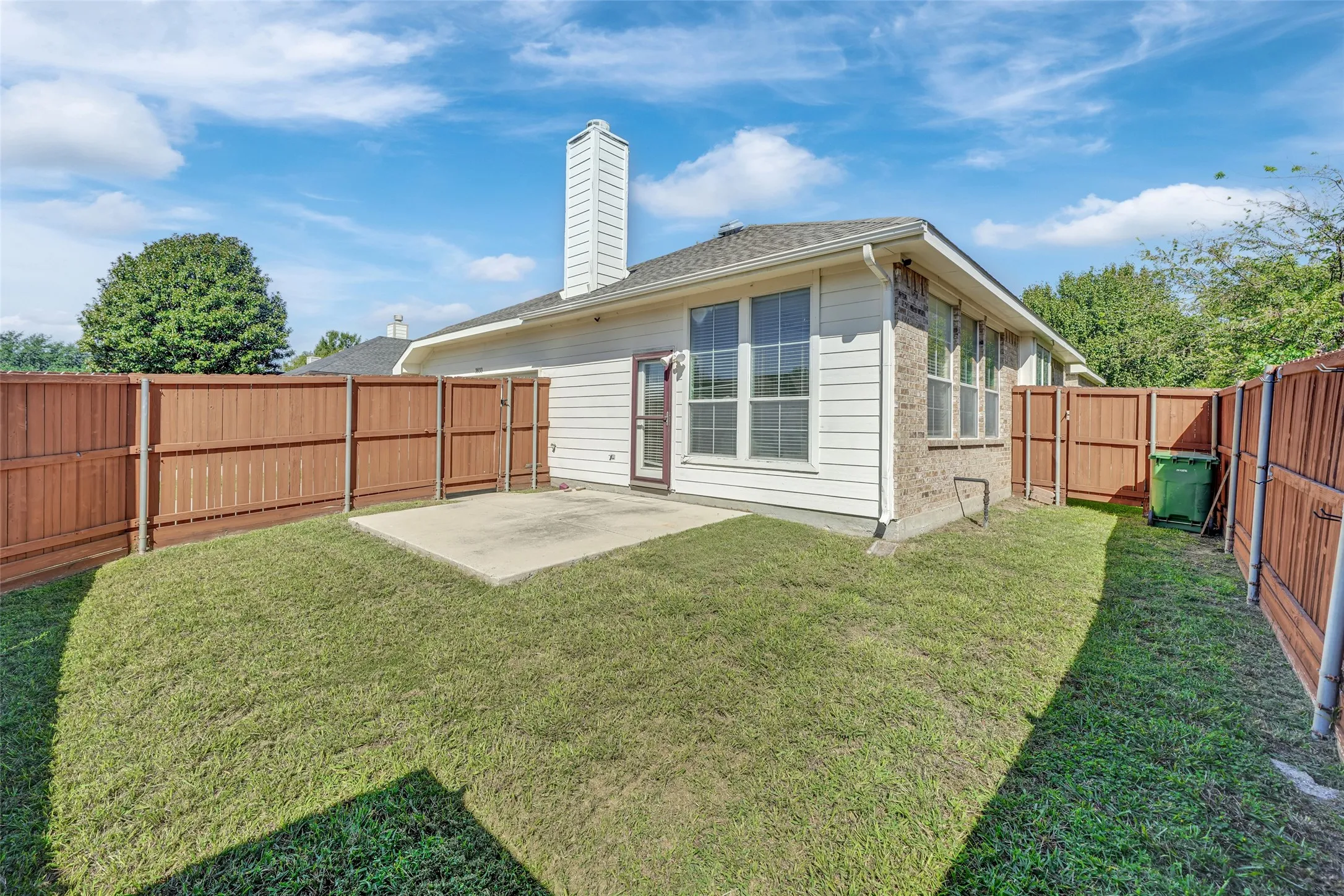 Enclosed backyard with a concrete patio, wood fencing, and a white siding exterior
