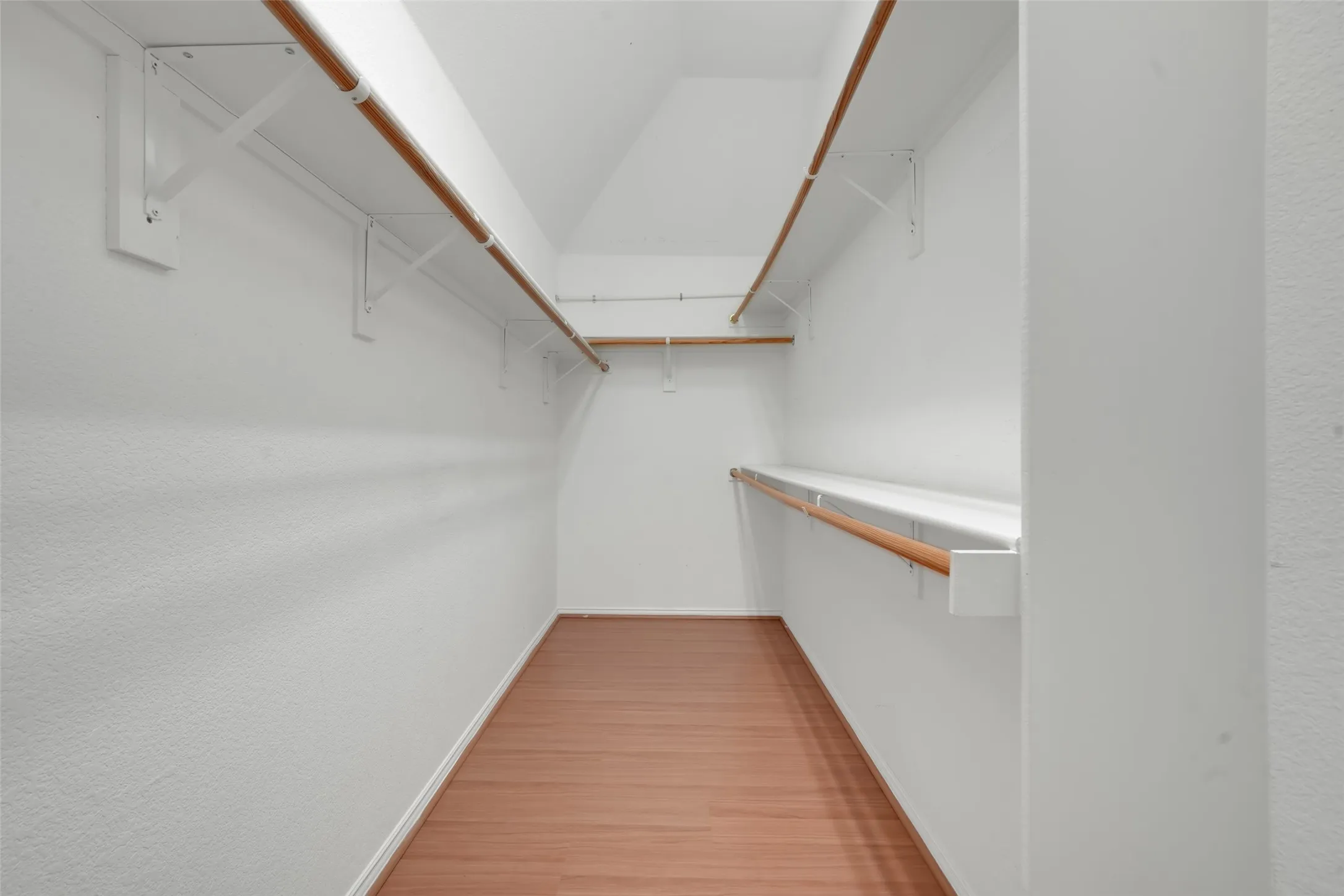 Walk-in closet with wood-finish flooring, white walls, and multiple levels of shelving and hanging rods