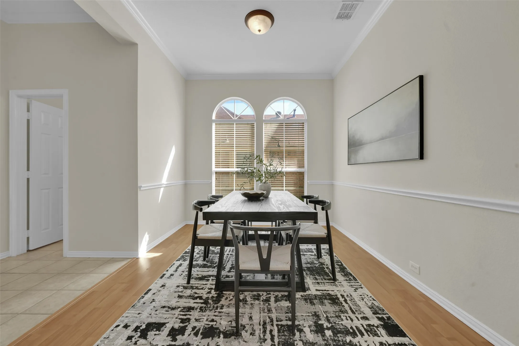Arched windows with horizontal blinds, neutral-toned walls, wood-finish flooring, and crown molding