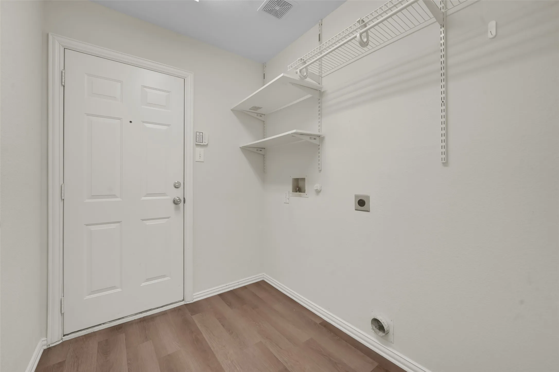 Wood-finish flooring, white paneled door, built-in shelving, and white walls