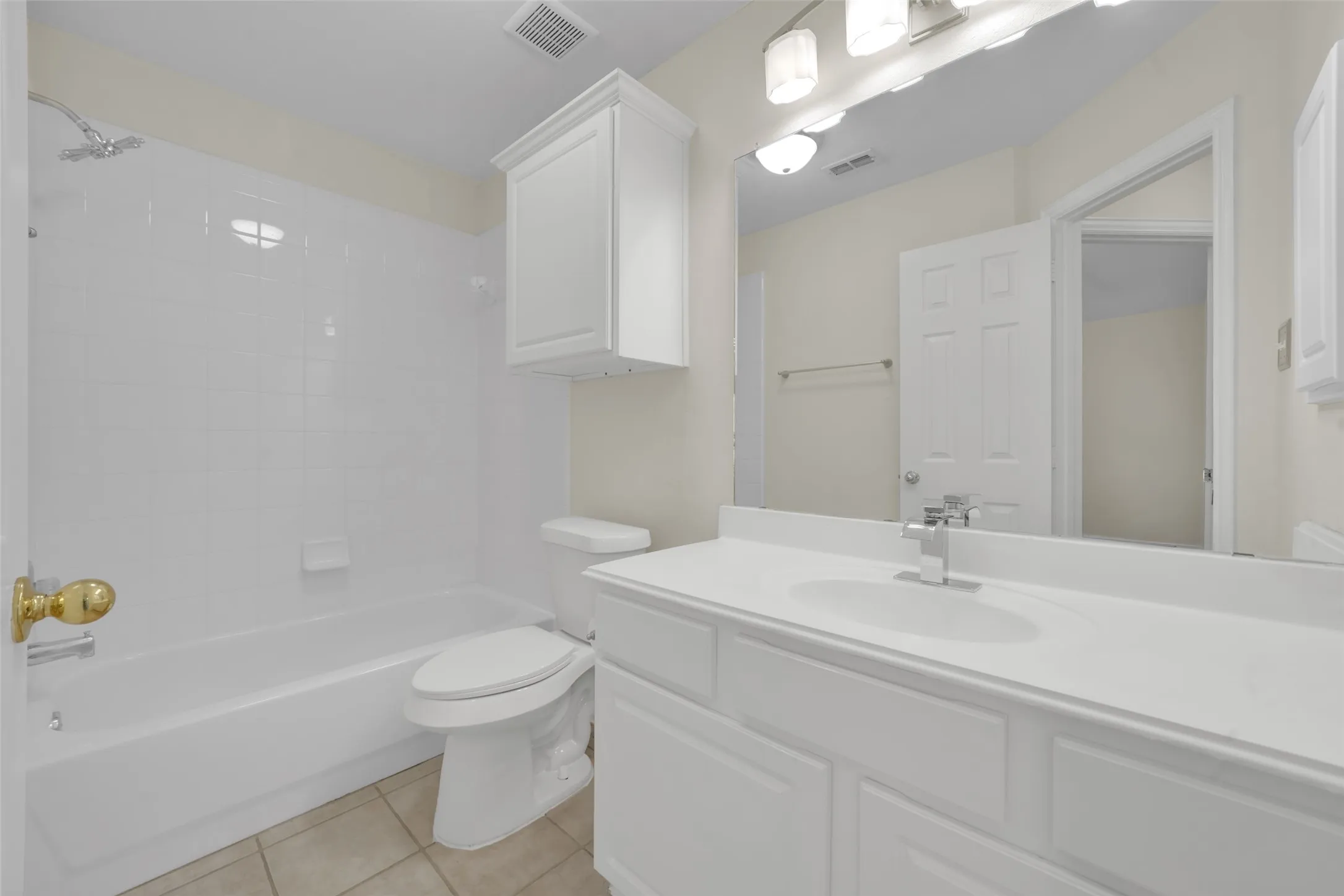 White tiled shower and tub combination, white vanity with integrated sink, chrome faucet, and overhead cabinet storage