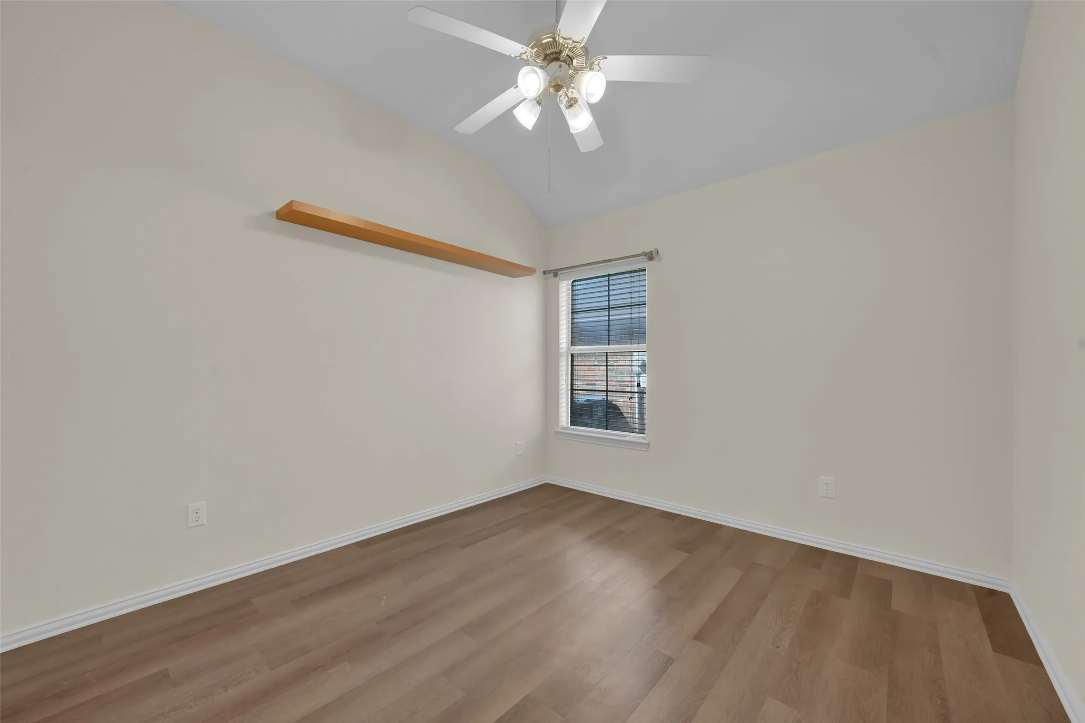 Vaulted ceiling, ceiling fan with light fixture, wood-finish flooring, built-in wall shelving, and window with blinds
