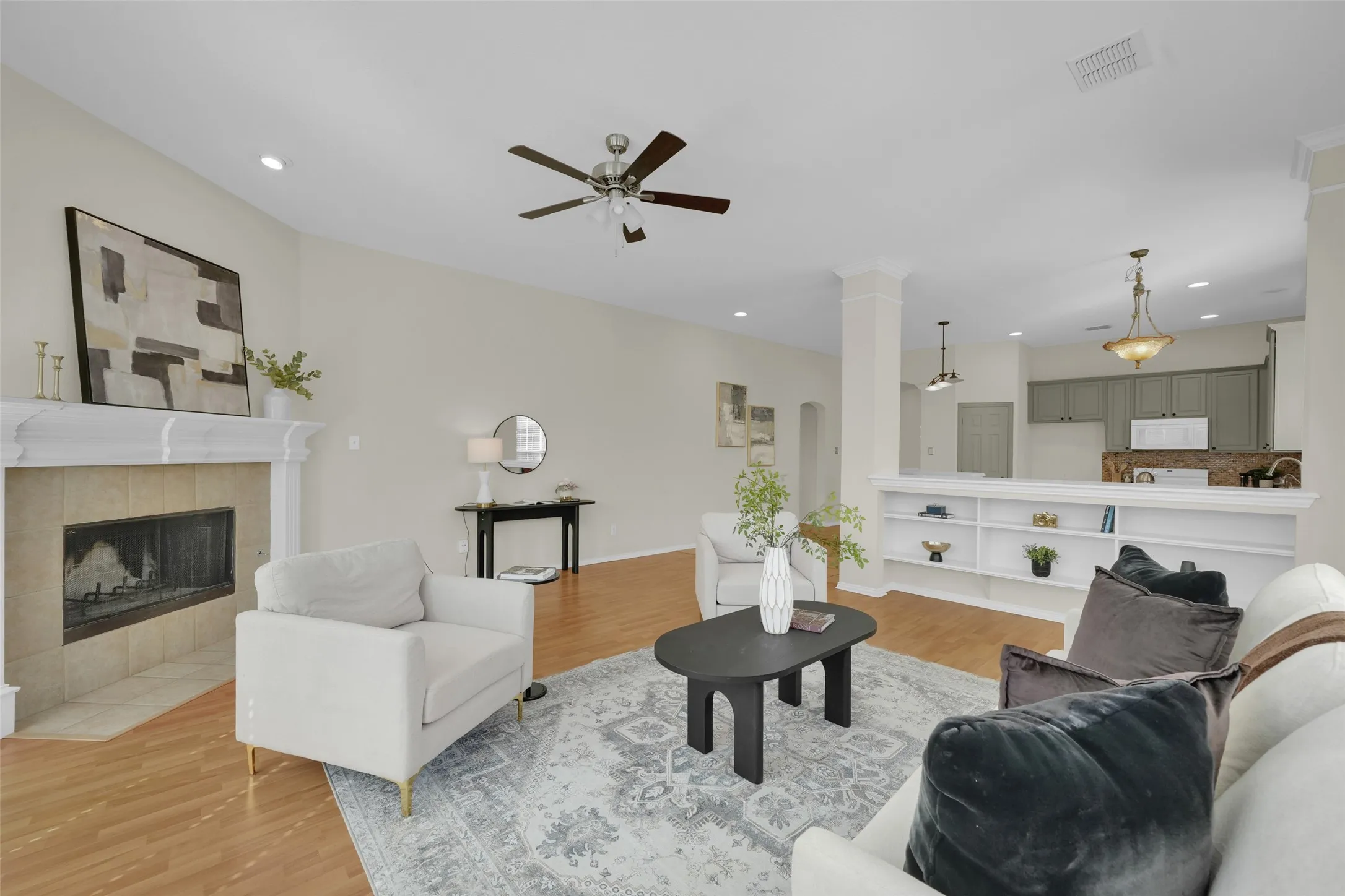 Vaulted ceiling with a ceiling fan, recessed lighting, tile-surround fireplace with a mantel, wood-finish flooring, and built-in shelving