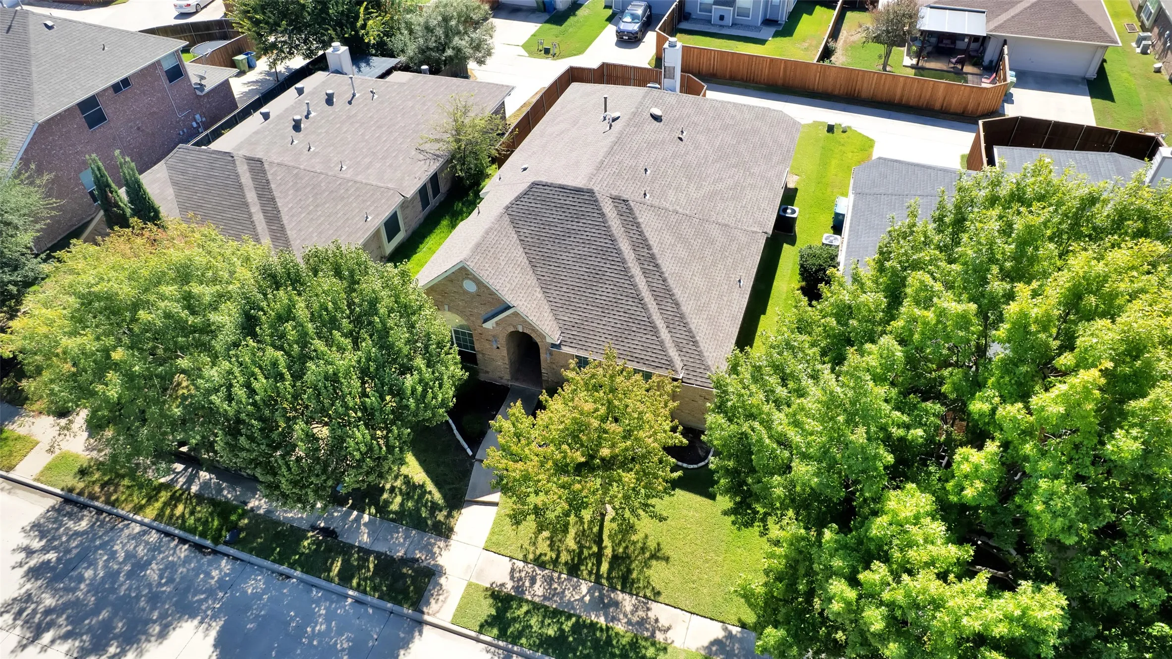 Traditional brick exterior with an arched entry, a gabled roof, a manicured lawn, and mature trees