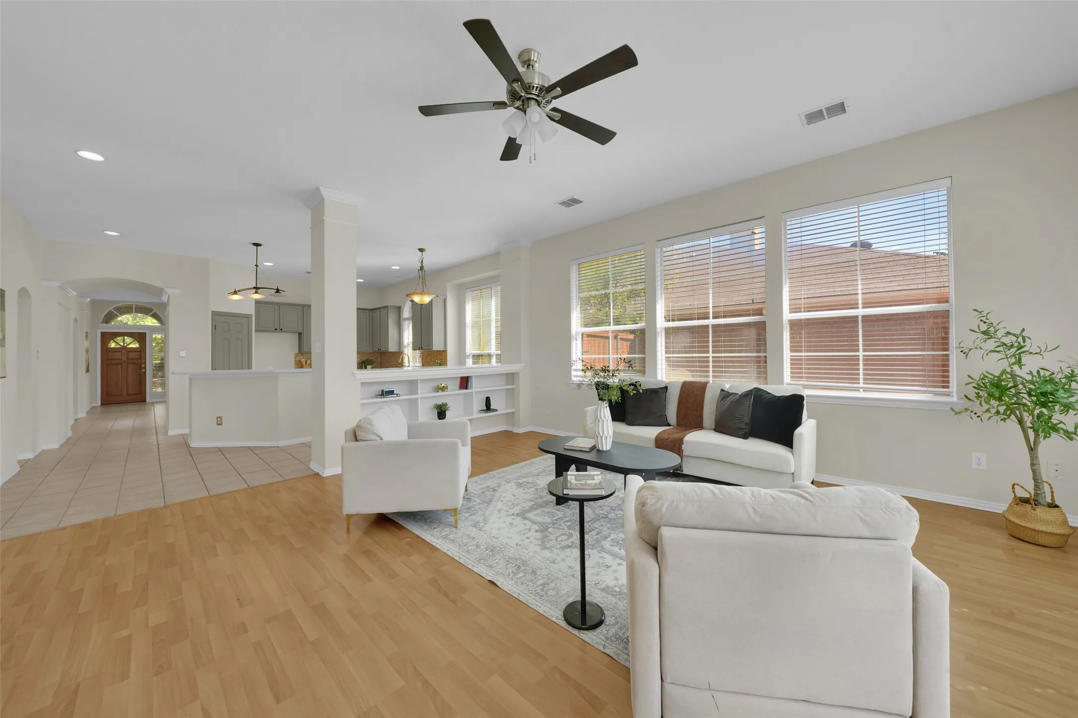 Living area with wood-finish flooring, built-in shelving, a ceiling fan, and multiple windows