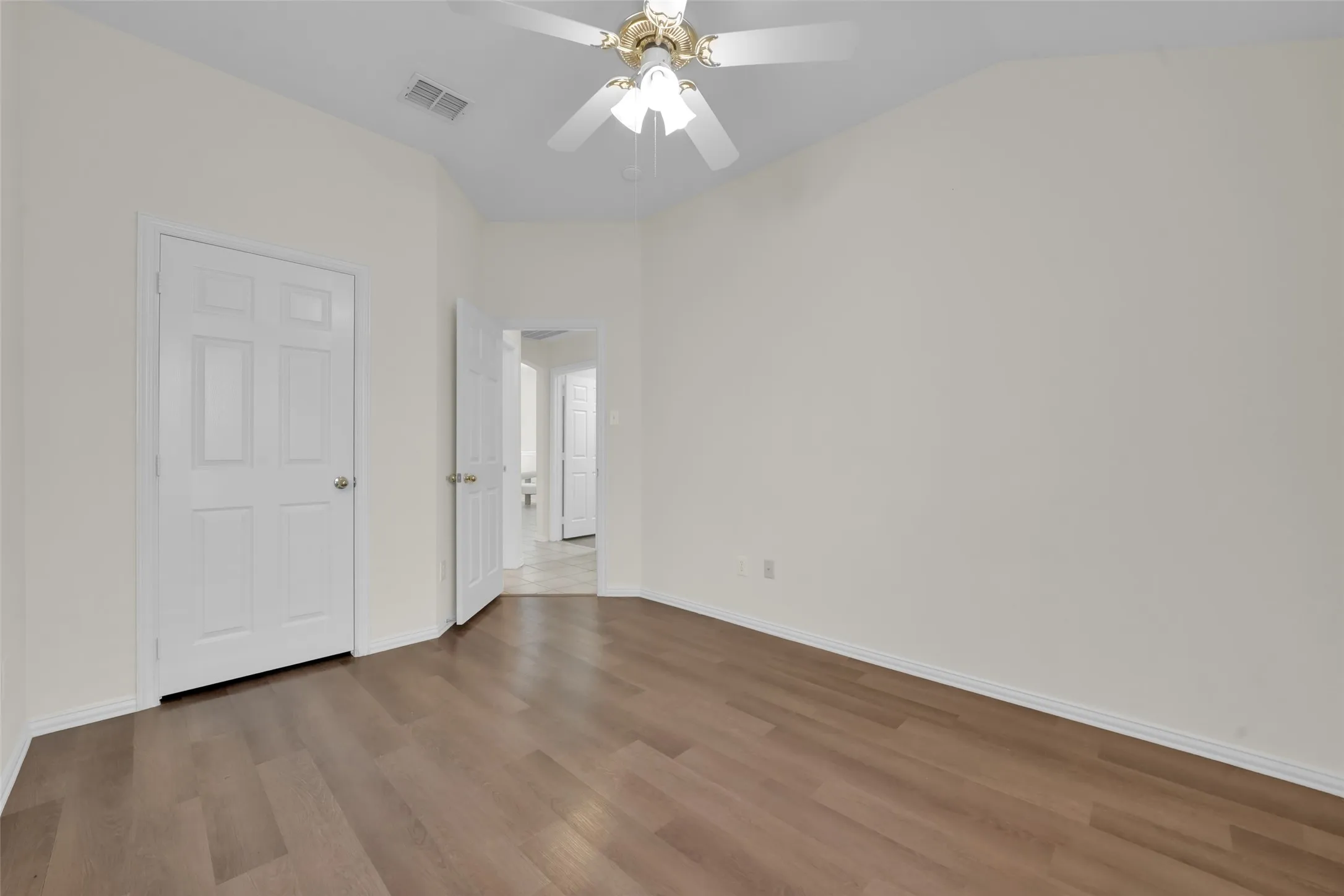 Vaulted ceiling with a ceiling fan, wood-finish flooring, and white paneled doors