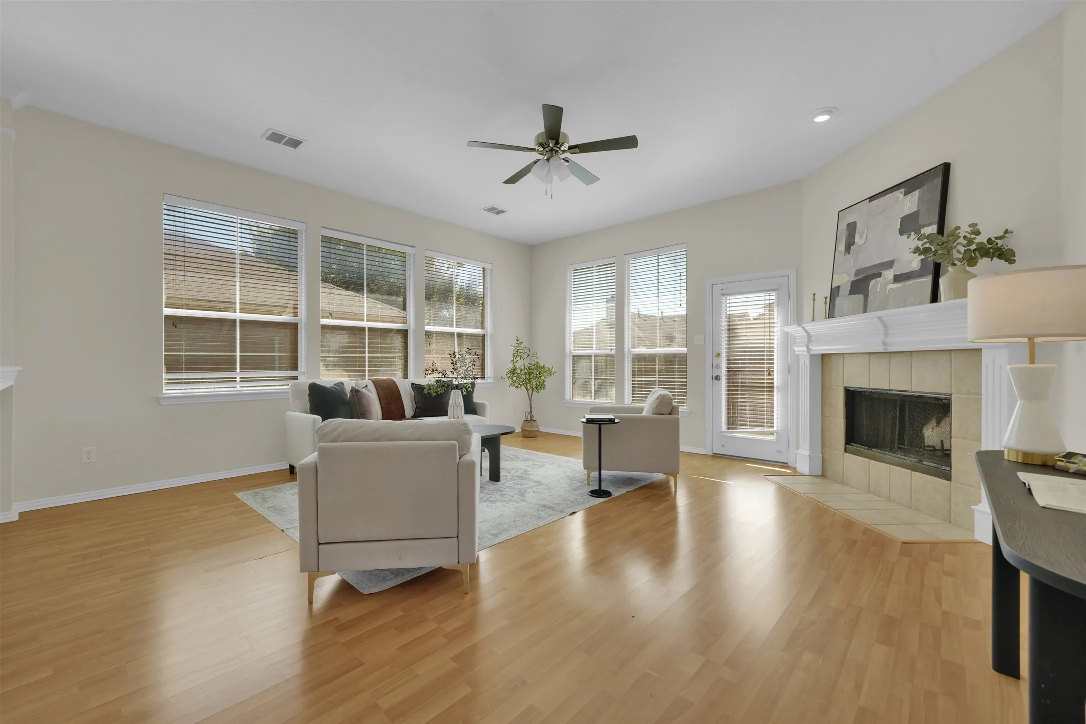 Bright living space featuring wood-finish flooring, multiple windows, a ceiling fan, and a fireplace with a tile surround and mantel