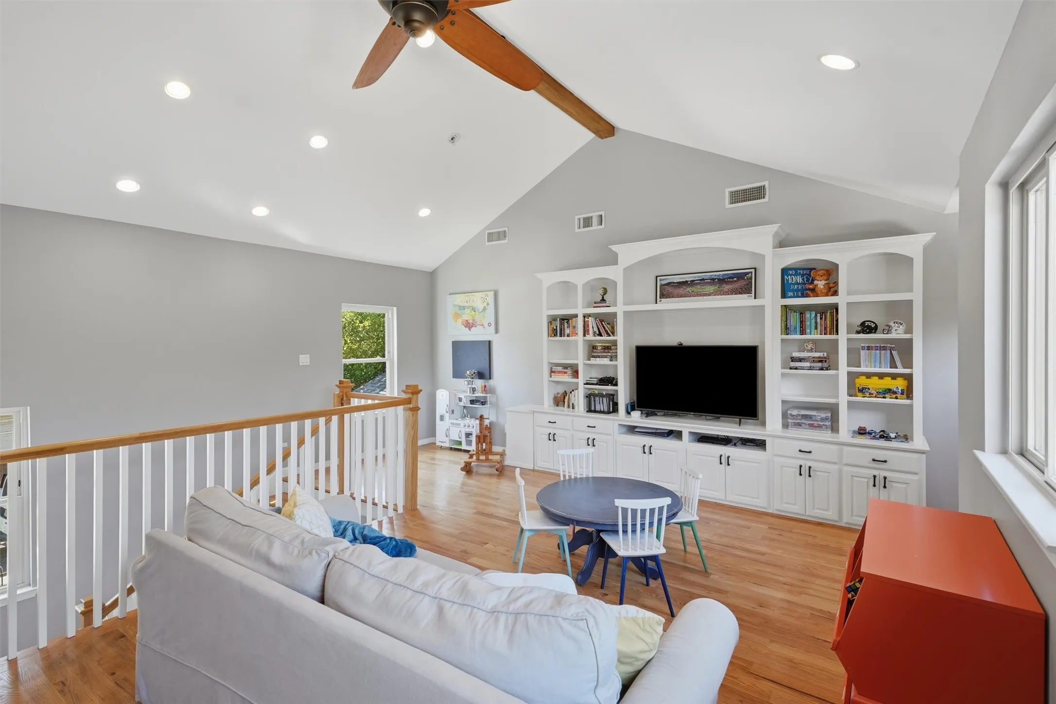 Spacious upstairs family room featuring vaulted ceilings with custom built-in media shelving, hardwood flooring, and a safety railing.