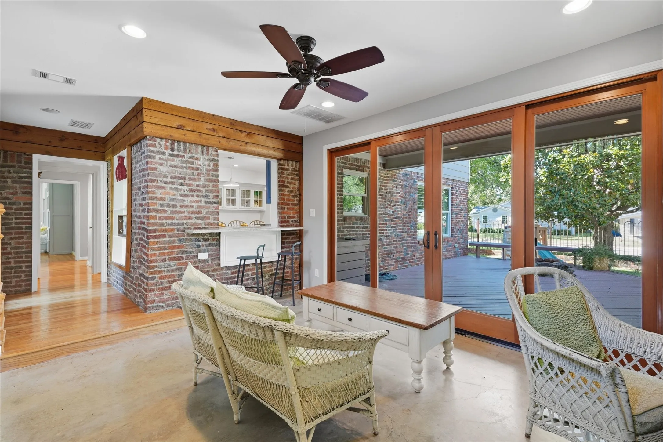 Alternate sunroom angle showing the pass-through breakfast bar connected to the kitchen. Highlights exposed brick walls, warm wood trim, and direct sliding glass door access to the back deck.