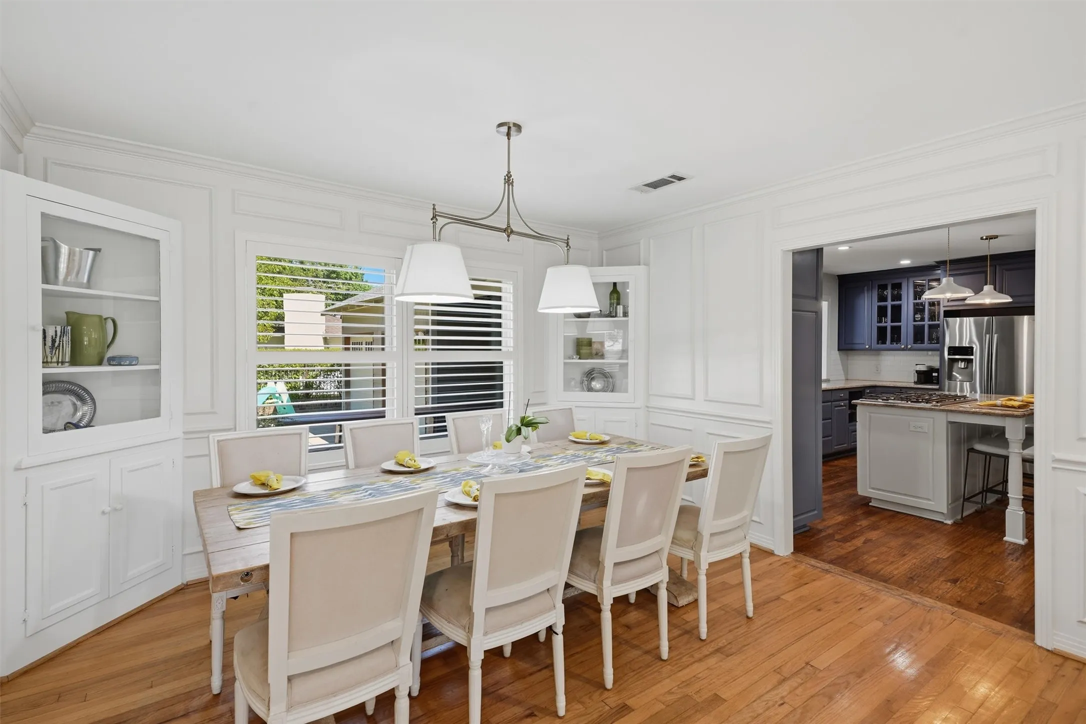 Elegant formal dining room with built-in display cabinets, wall wainscoting, and seamless flow into the kitchen.