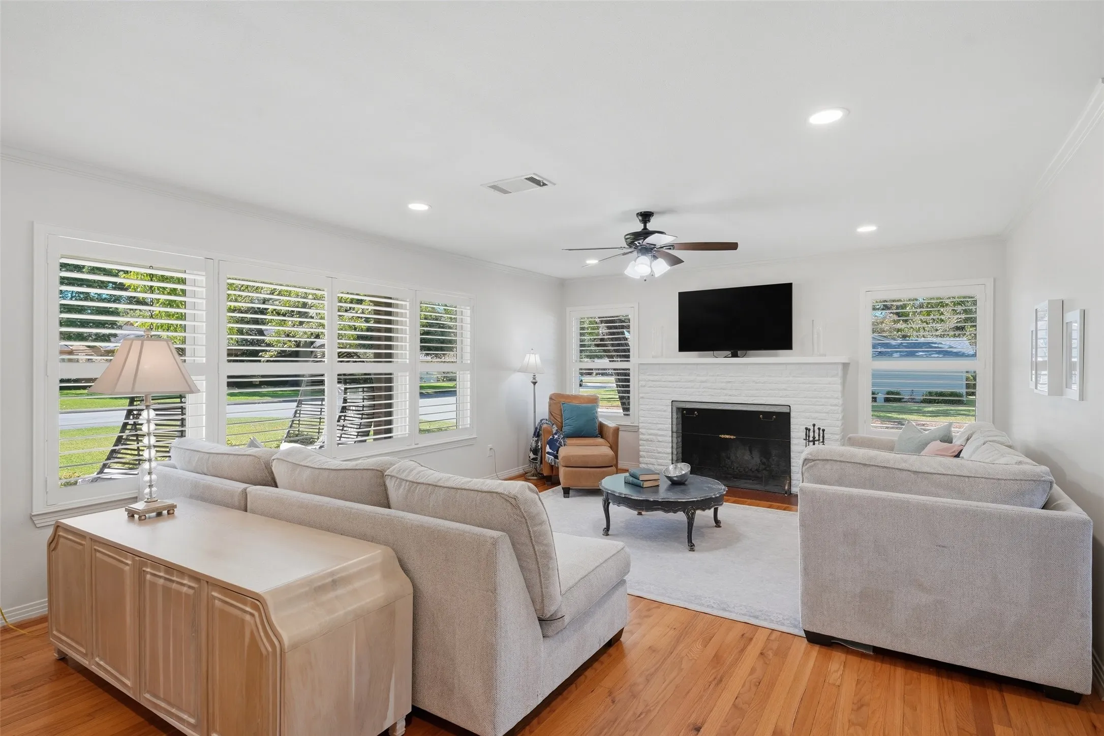 Bright, spacious living room with warm hardwood floors, Plantations shutters frame large windows for ample natural light.