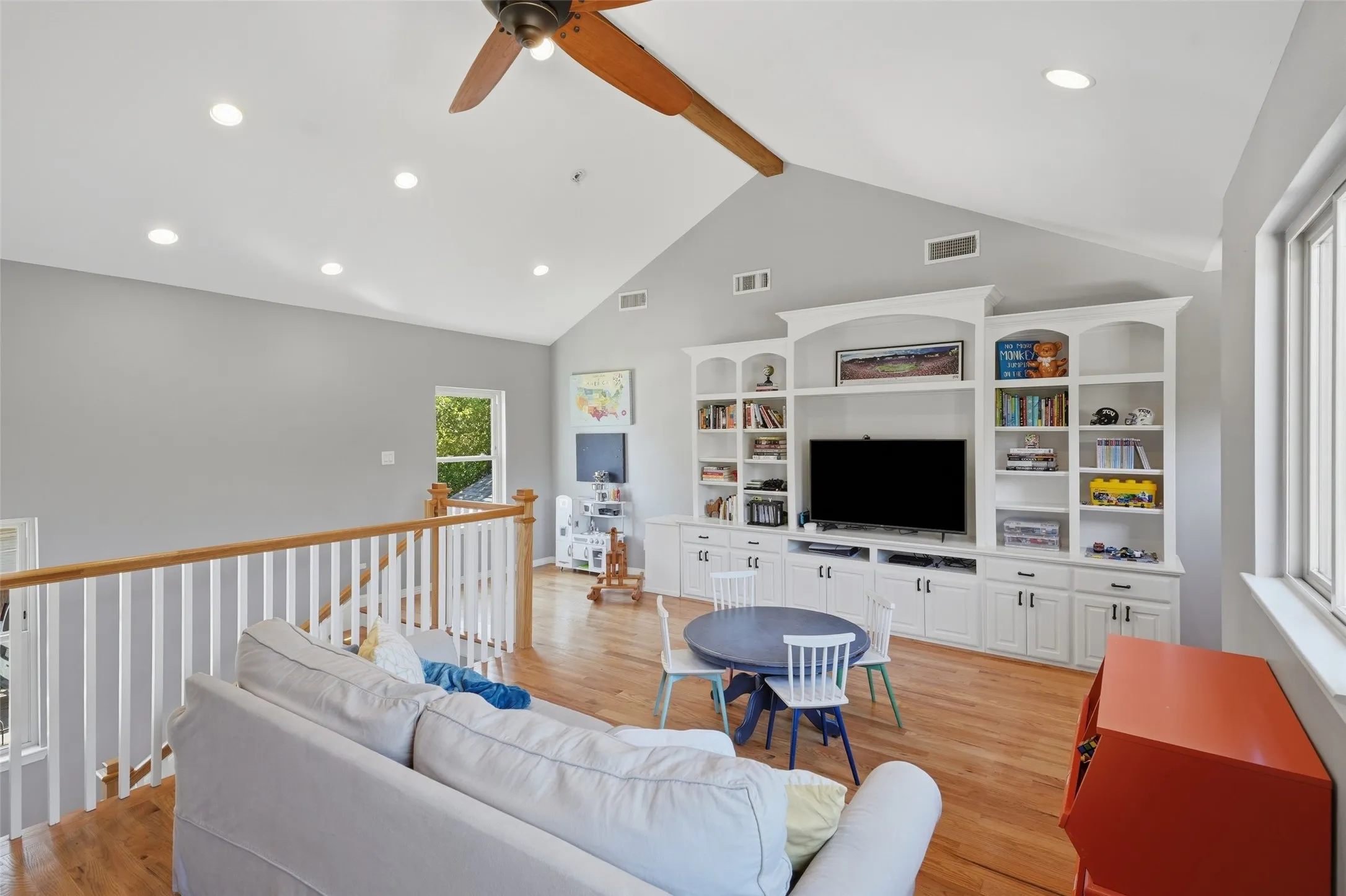 Spacious upstairs family room featuring vaulted ceilings with custom built-in media shelving, hardwood flooring, and a safety railing.